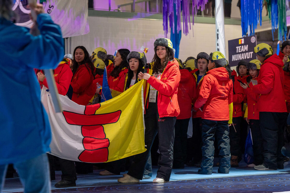 Young athletes hold a Nunavut flag as they enter the ceremonies