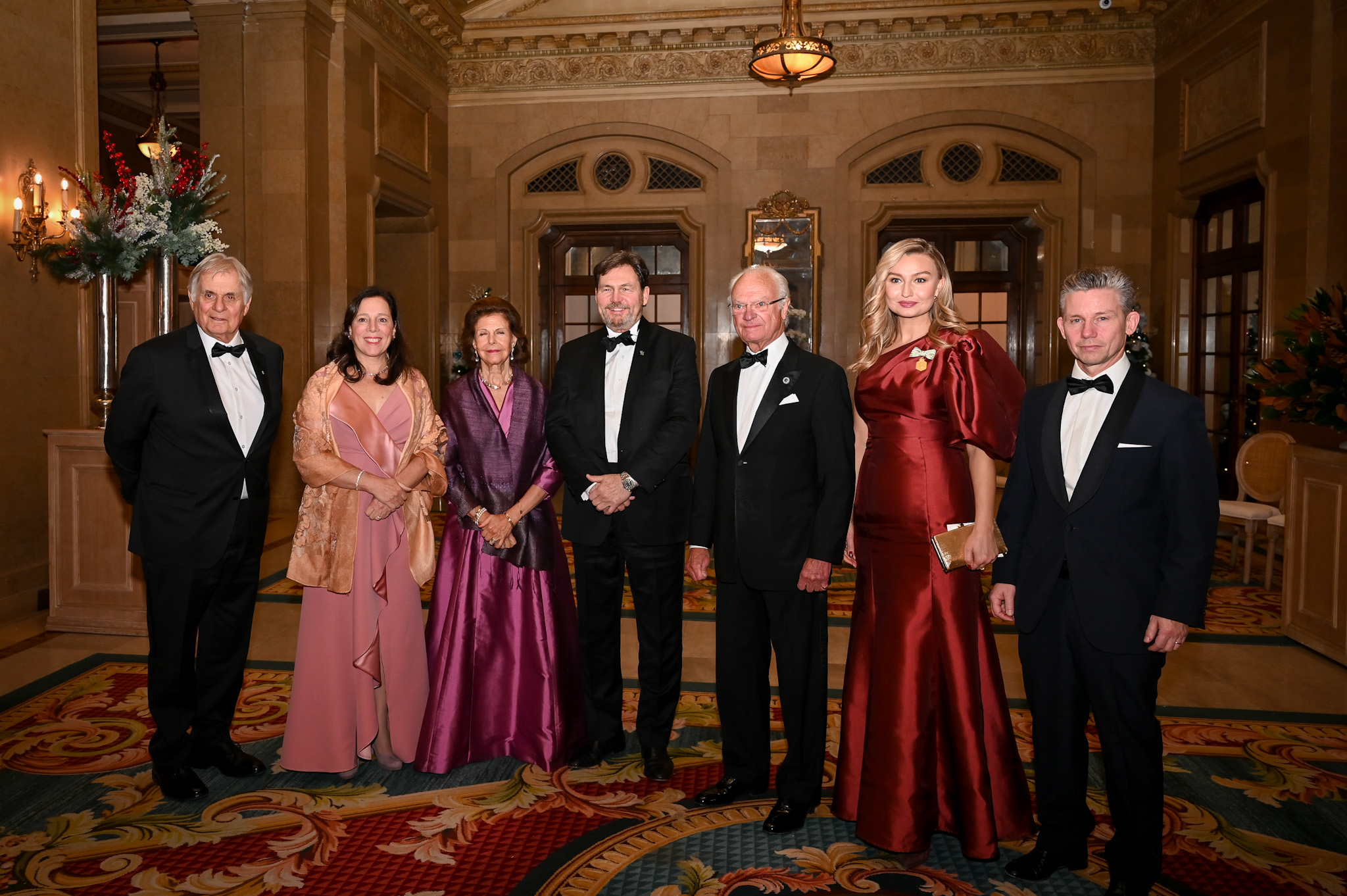 De gauche à droite : M. Whit Fraser, l'honorable Catherine Mandeville, Sa Majesté la reine Silvia de Suède, le très honorable Richard Wagner, Sa Majesté le roi Carl XVI Gustaf de Suède, la vice-Première ministre suédoise Ebba Busch et un homme en costume, tous vêtus d'une tenue formelle.