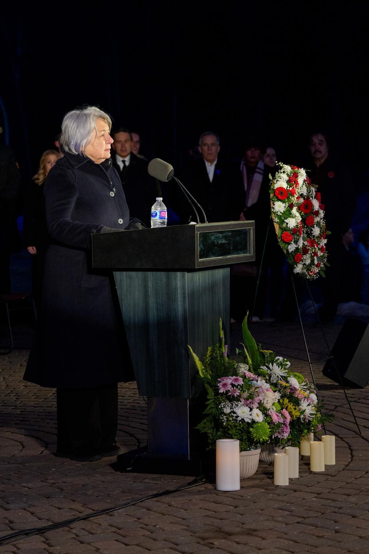 Governor General Mary Simon speaking at a podium. There are flowers and candles on the ground.