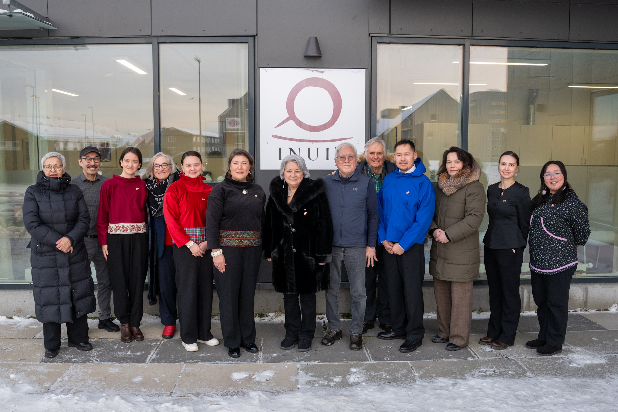 Governor General Mary Simon and Mr. Whit Fraser standing outside with a group of people. A sign behind them has the word 'Inuit'.