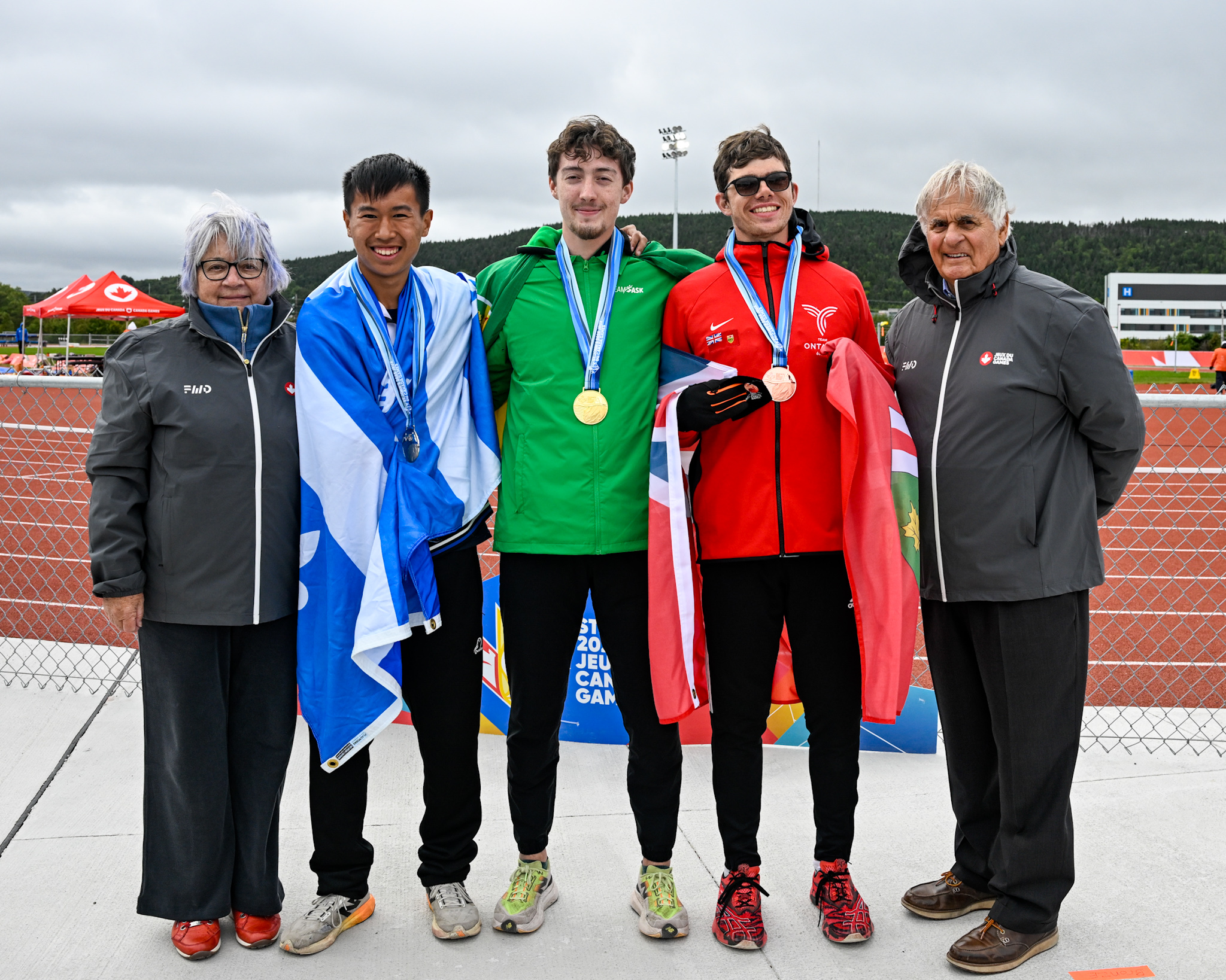 Governor General Mary Simon and Mr. Whit Fraser posing with 3 athletes who are wearing medals around their necks. 
