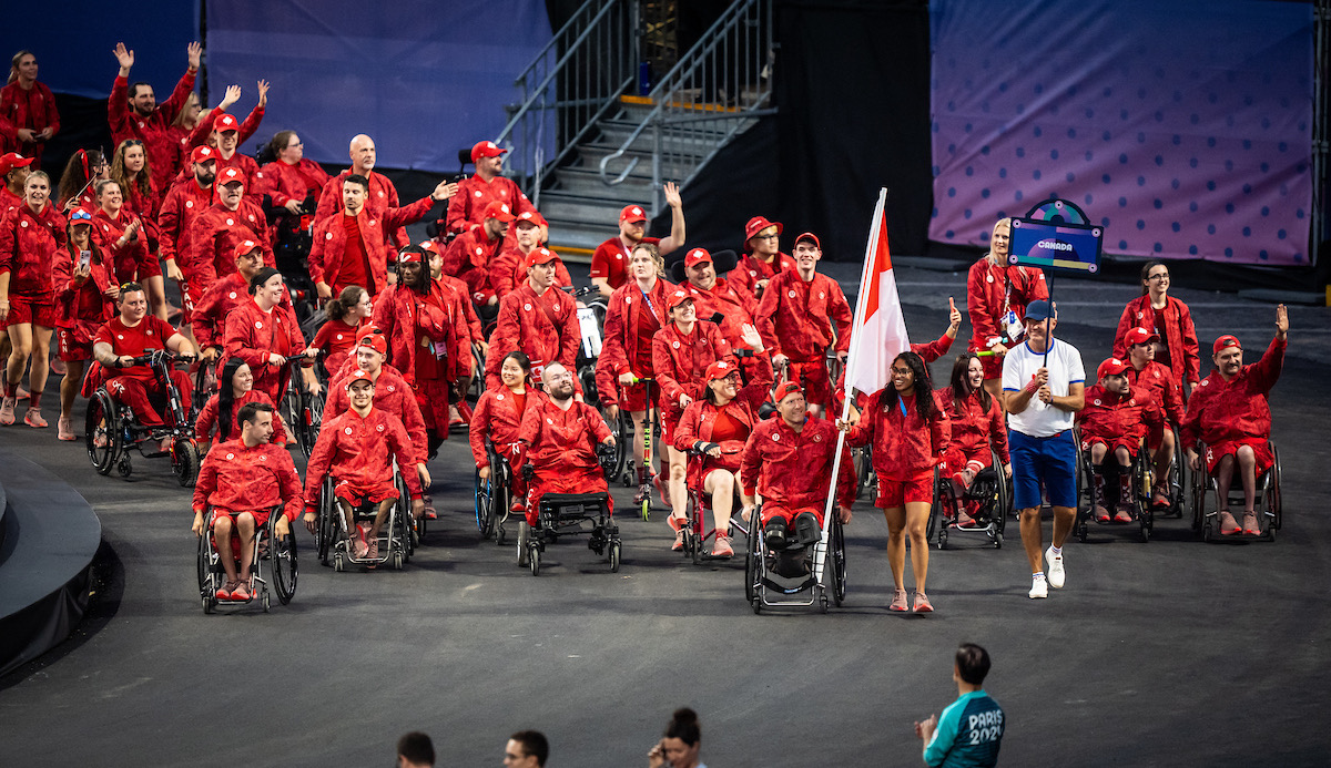 Deux porte-drapeaux, Katarina Roxon et Pat Anderson, mènent l'équipe canadienne lors de la cérémonie d'ouverture des Jeux paralympiques à Paris, France. L'équipe avance fièrement avec leurs drapeaux.