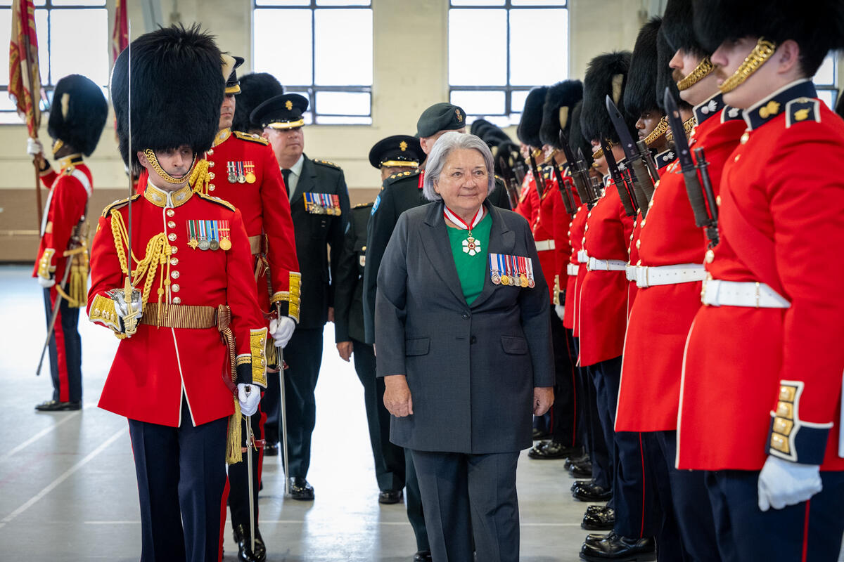 Governor General Mary Simon walking past a row of Canadian Grenadier Guards inside a large gymnasium.