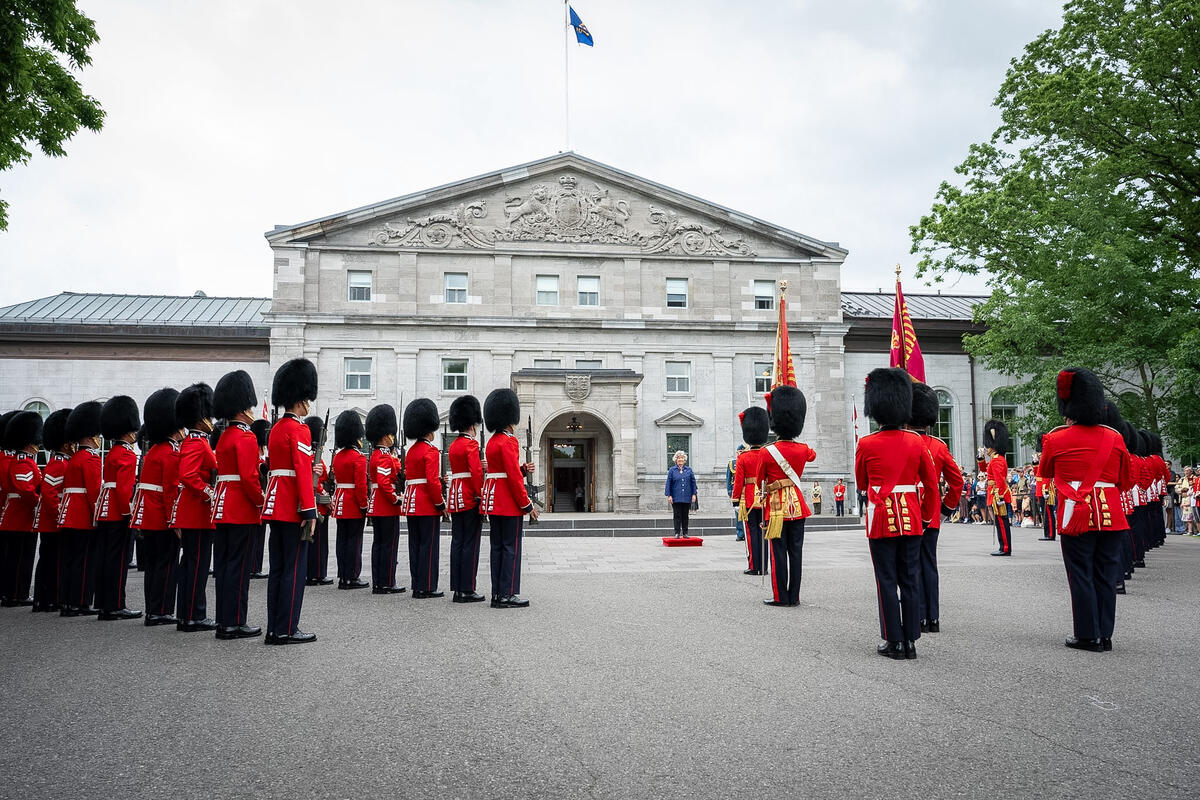 Governor General Arbour standing on a small platform set up in front of Rideau Hall. The members of the Ceremonial Guard are facing her.