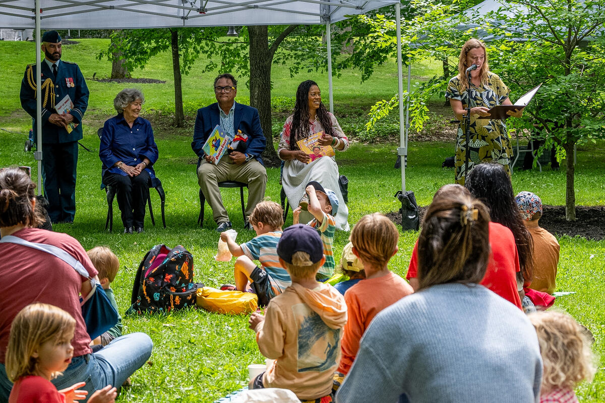Governor General Arbour and three other people are seated in front a group of kids for storytime.