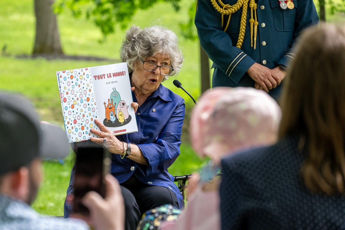 Governor General Arbour holding up a children's book as she reads to the audience outside.