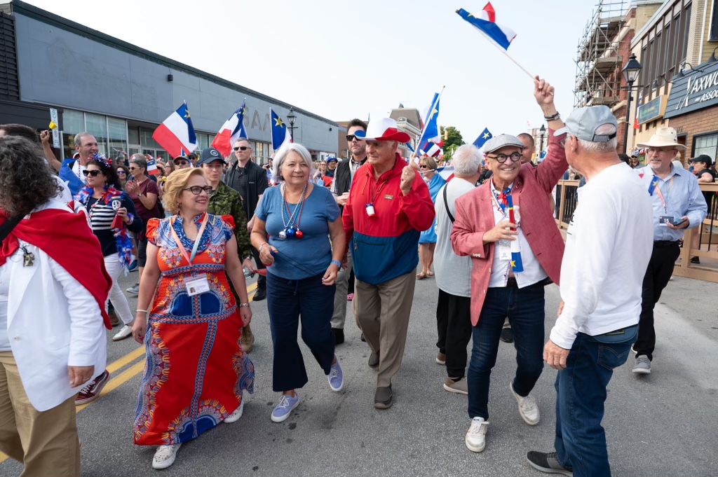 La gouverneure générale Mary Simon et M. Whit Fraser marchent avec une foule de gens à l'extérieur, participant aux festivités de la Fête nationale de l'Acadie.