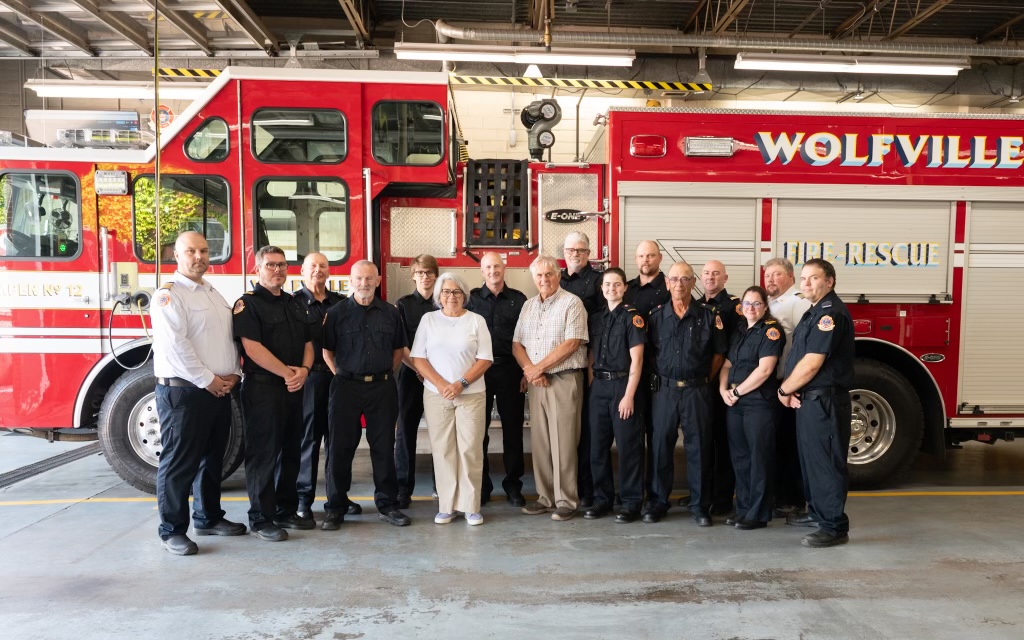 La gouverneure générale Mary Simon pose avec des membres du Service d'incendie de Wolfville. Il y a un camion de pompiers en arrière-plan.