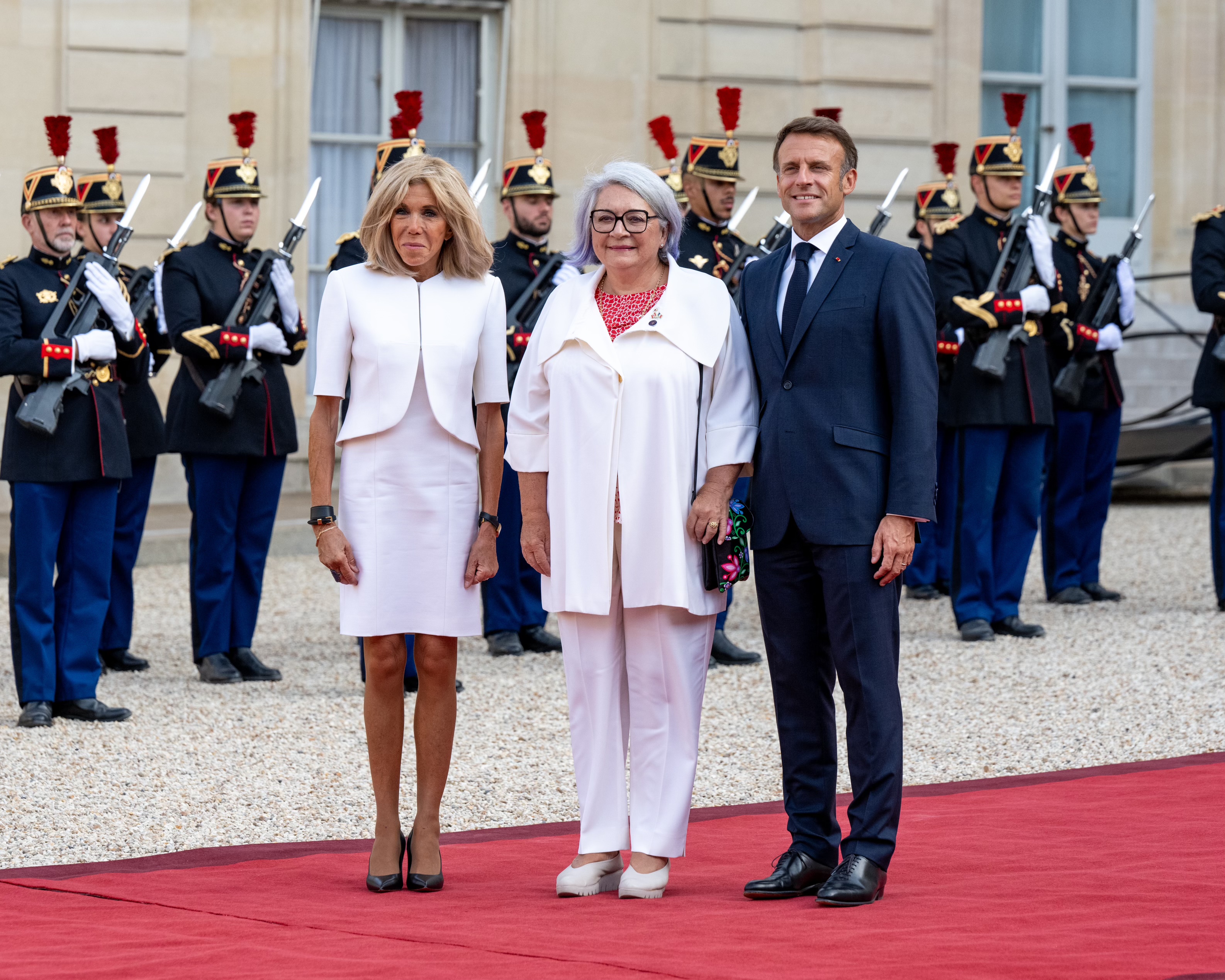 La gouverneure générale du Canada Mary Simon se tient entre le Président Emmanuel Macron et sa femme Brigitte Macron. Ils sourient.