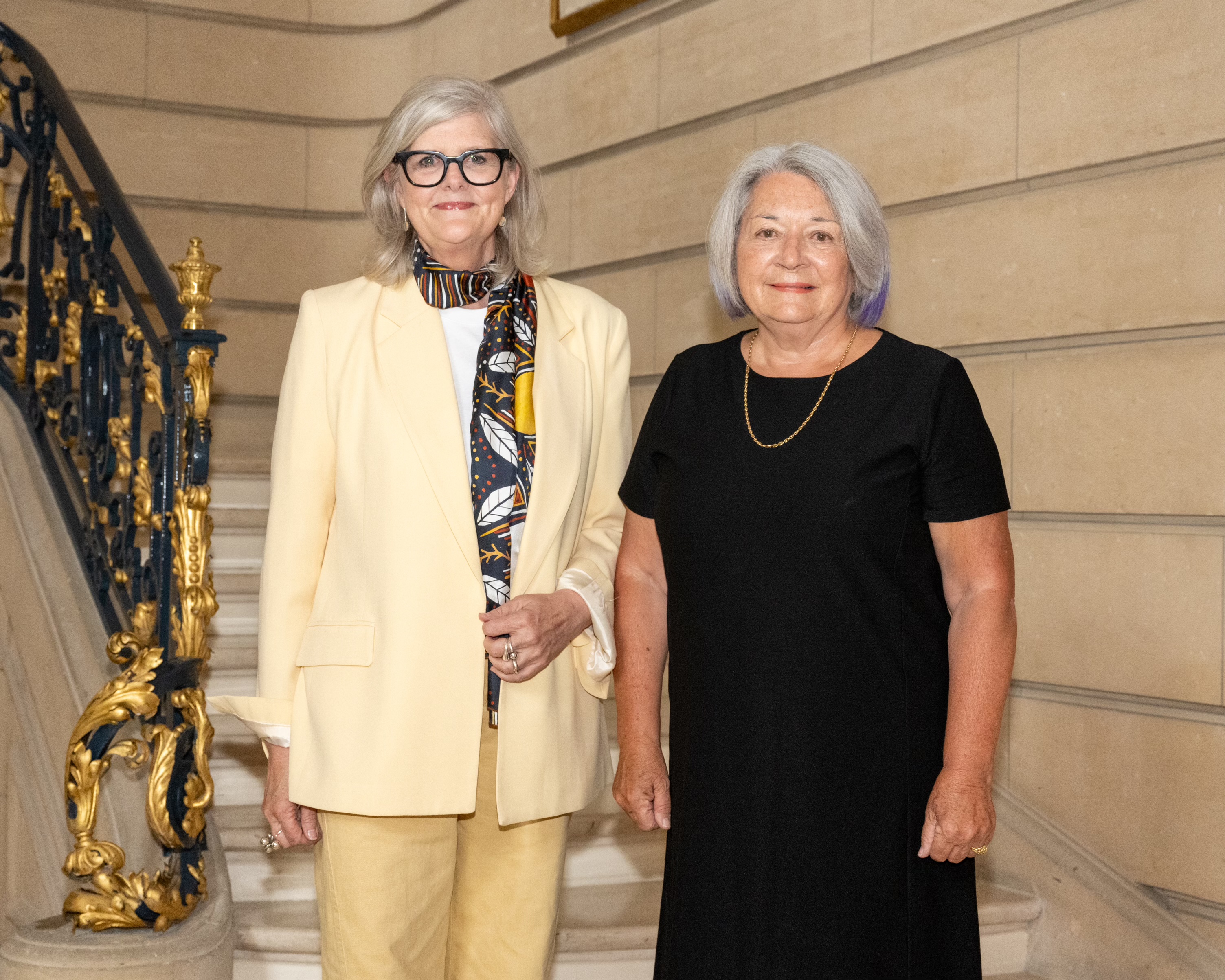 La gouverneure générale d'Australie, Sam Mostyn, et la gouverneure générale du Canada, Mary Simon, posant sur un escalier avec une rampe ornée de motifs dorés et noirs. Elles sourient.