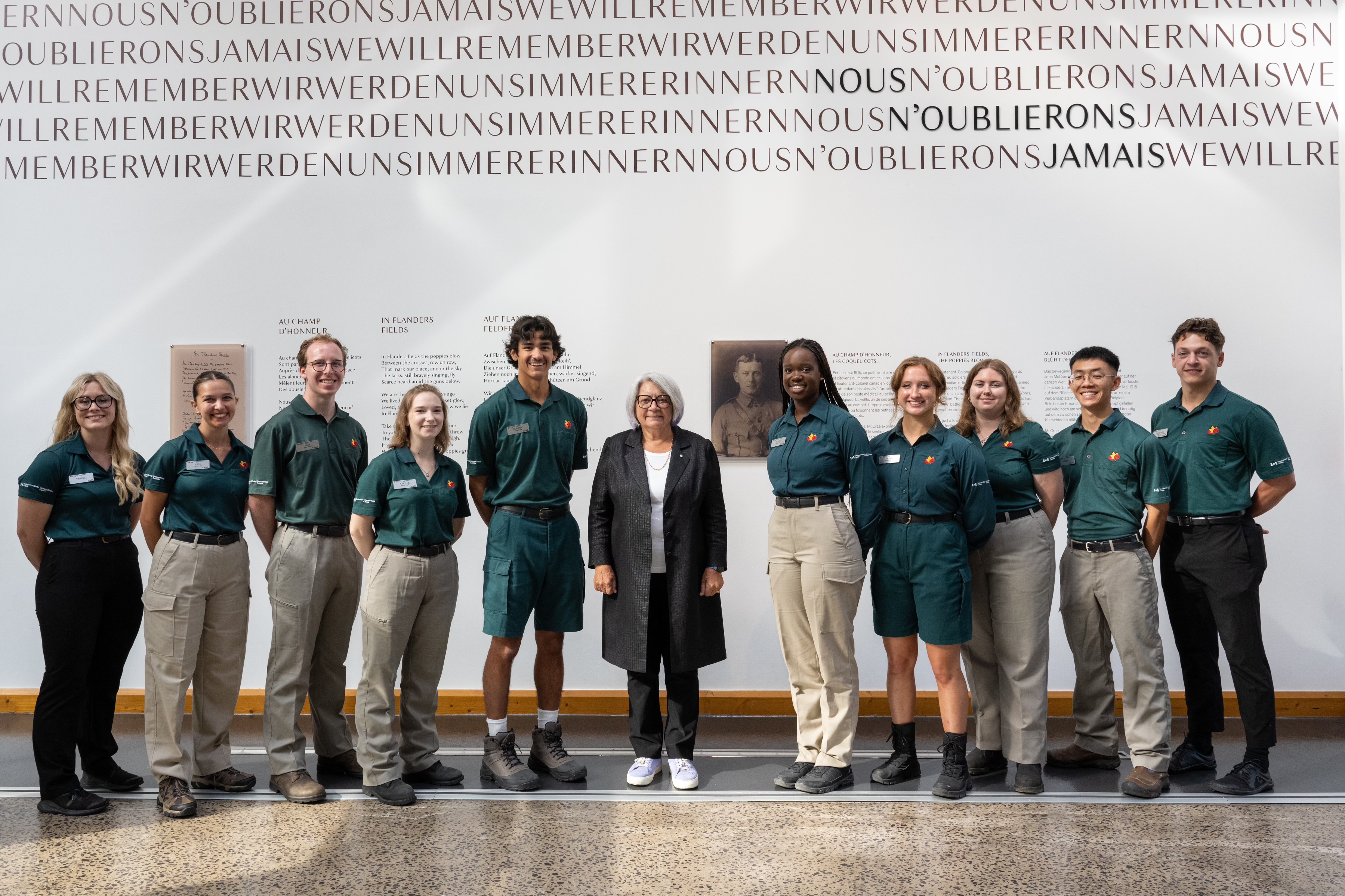 The Governor General of Canada Mary Simon in standing in line with a group of people in front of a wall with French text. 