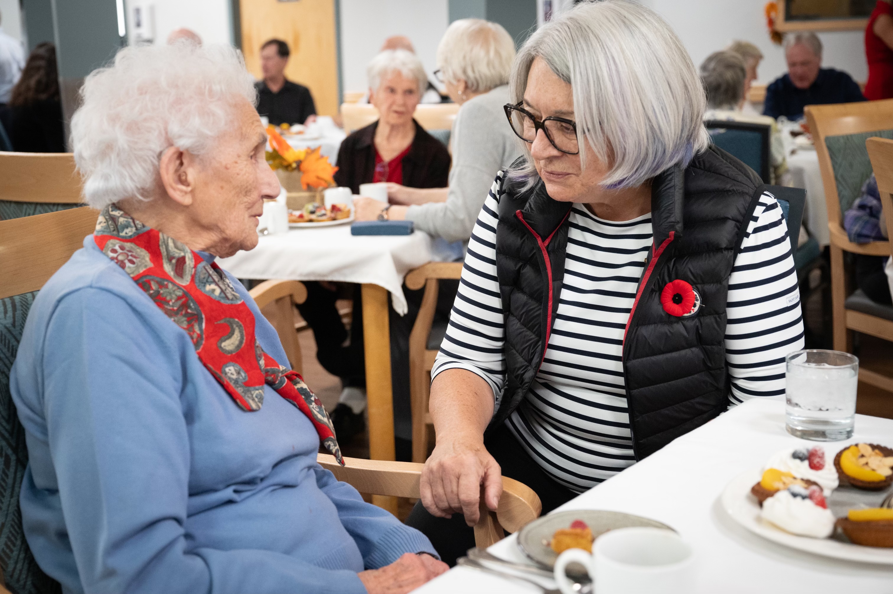 The Governor General chats with a woman. They are seated at a dining table.