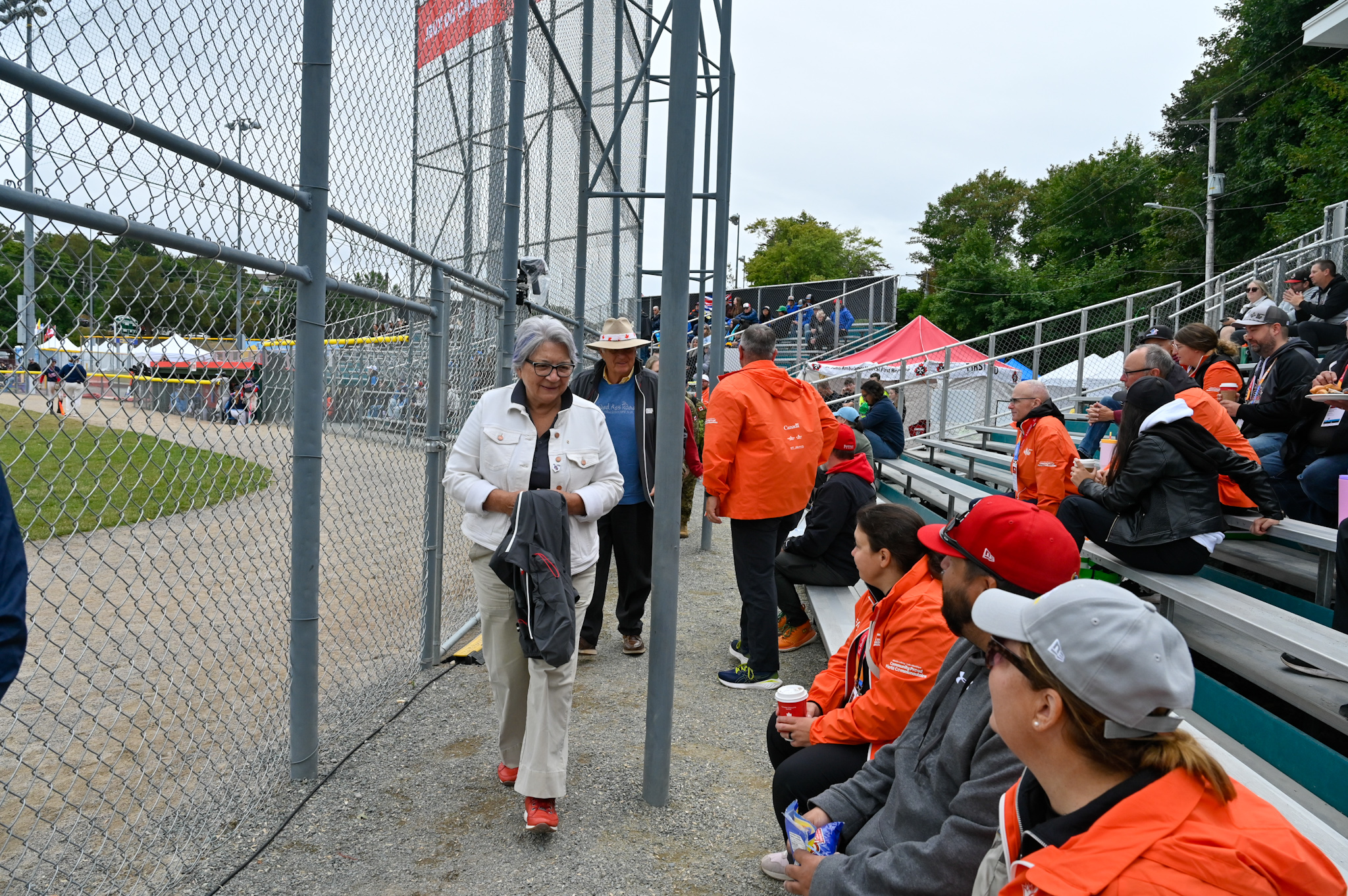 Governor General Mary Simon walking by a a group of people sitting in the stands at a baseball game.