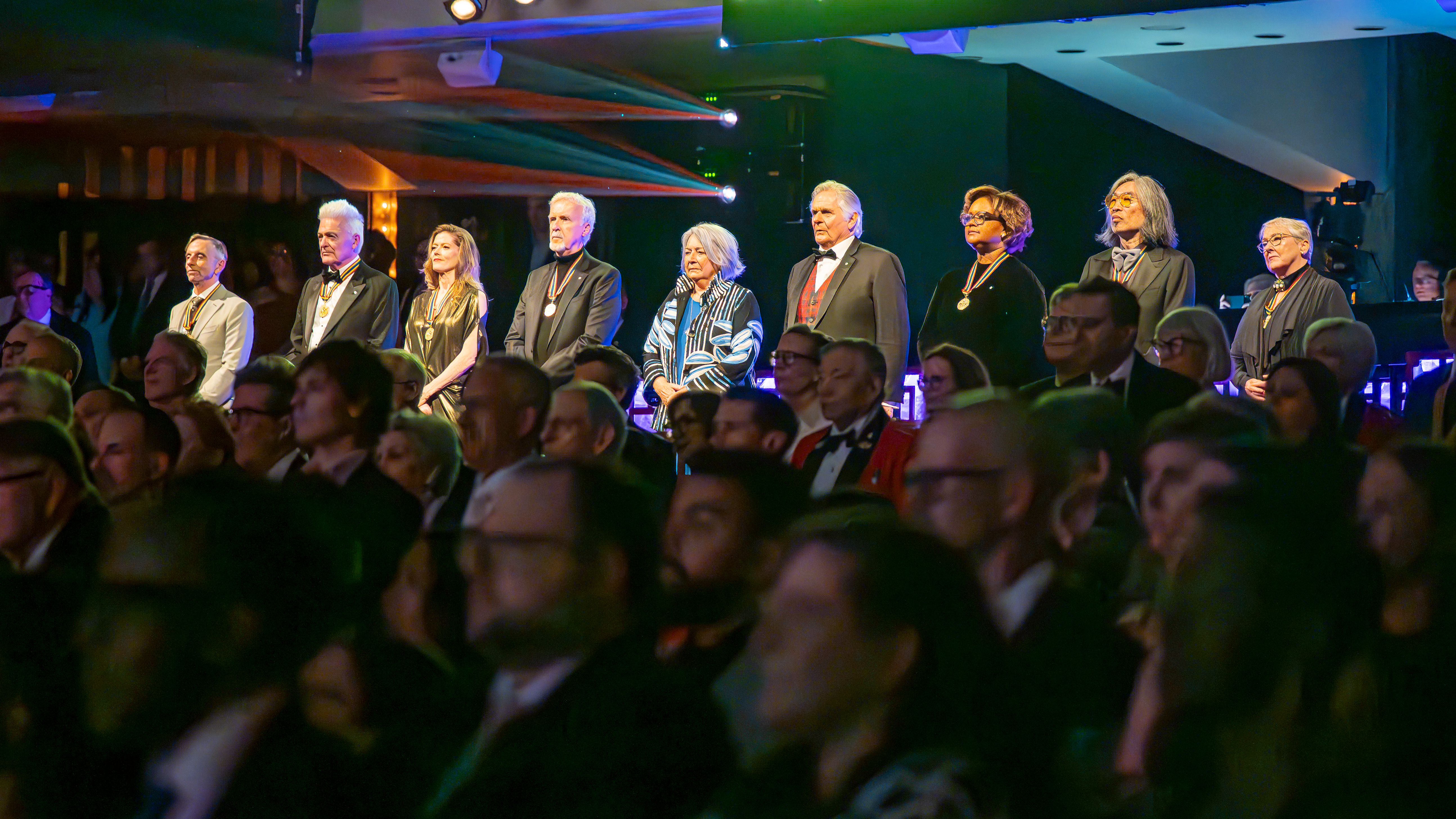 Governor General Mary Simon and Mr. Whit Fraser standing with laureates in the theatre of the National Arts Centre during the Governor General Performing Arts awards show.