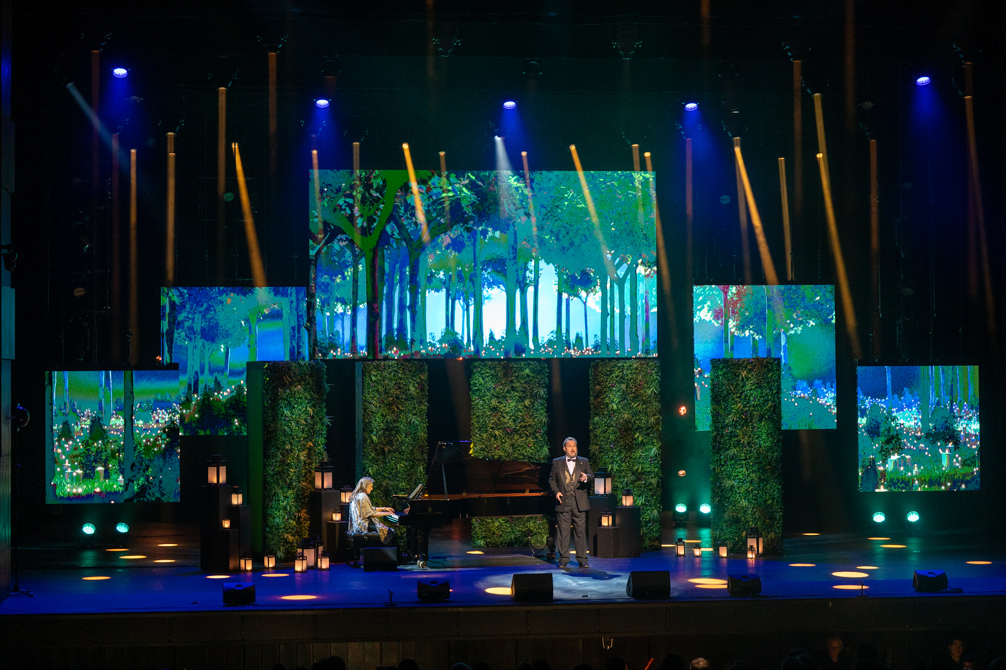 A pianist and one other person are onstage at the National Art Centre as part of the Governor General Performing Arts Awards show. There are several lanterns, screens and green backdrops on the stage. 