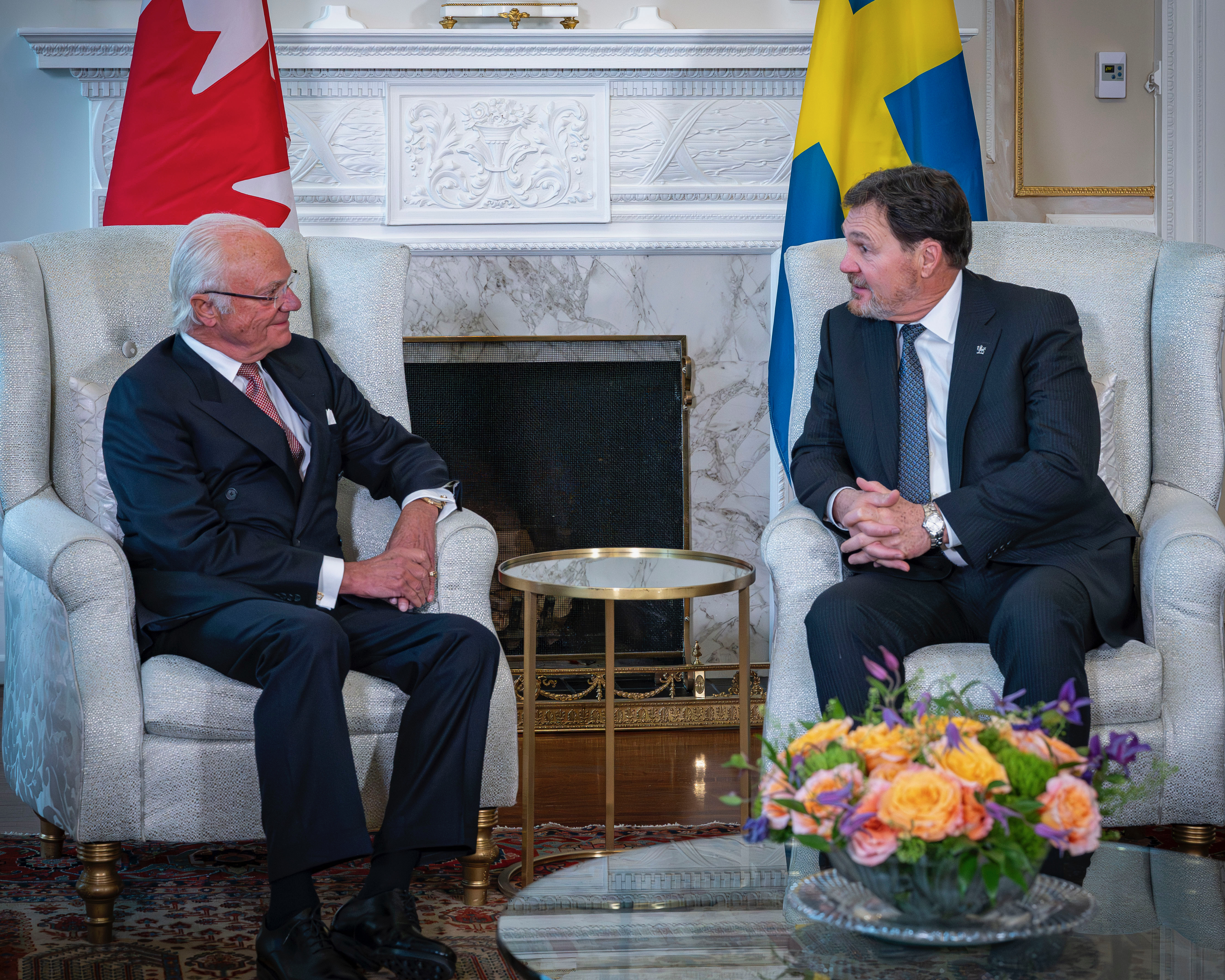 Sa Majesté le roi Carl XVI Gustaf assis en face du très honorable Richard Wagner, C.P., juge en chef du Canada et adjoint du gouverneur général. Une grande cheminée se trouve derrière eux.