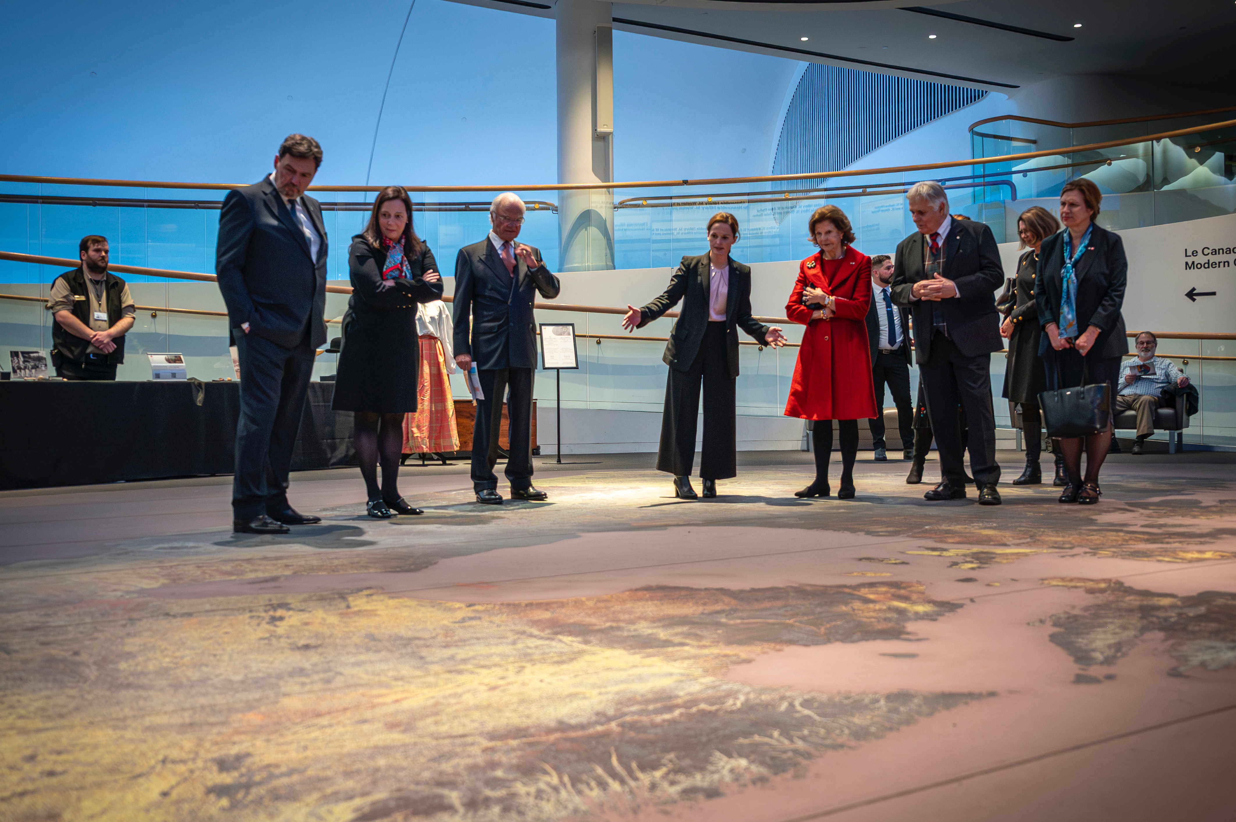 Un membre du personnel du musée montre une grande exposition au sol à Leurs Majestés le roi Carl XVI Gustaf et la reine Silvia de Suède, au très honorable Richard Wagner, à l'honorable Catherine Mandeville et à M. Whit Fraser.