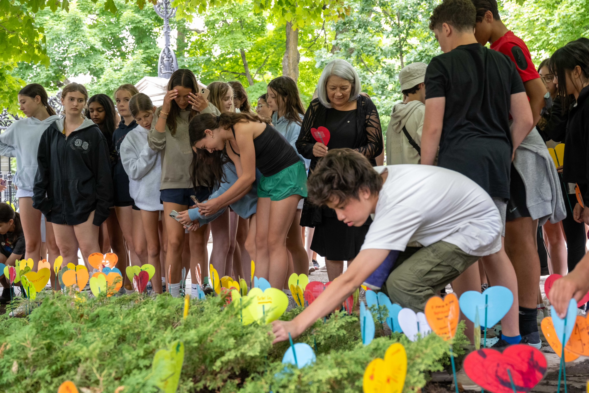 Governor General Mary Simon is surrounded by young students who are placing their cardboard hearts in the garden.