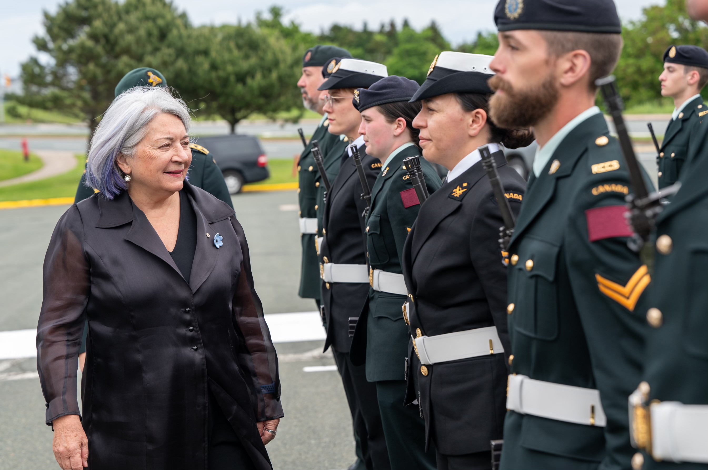 Governor General Simon walking past a row of people in uniform. They are outside.