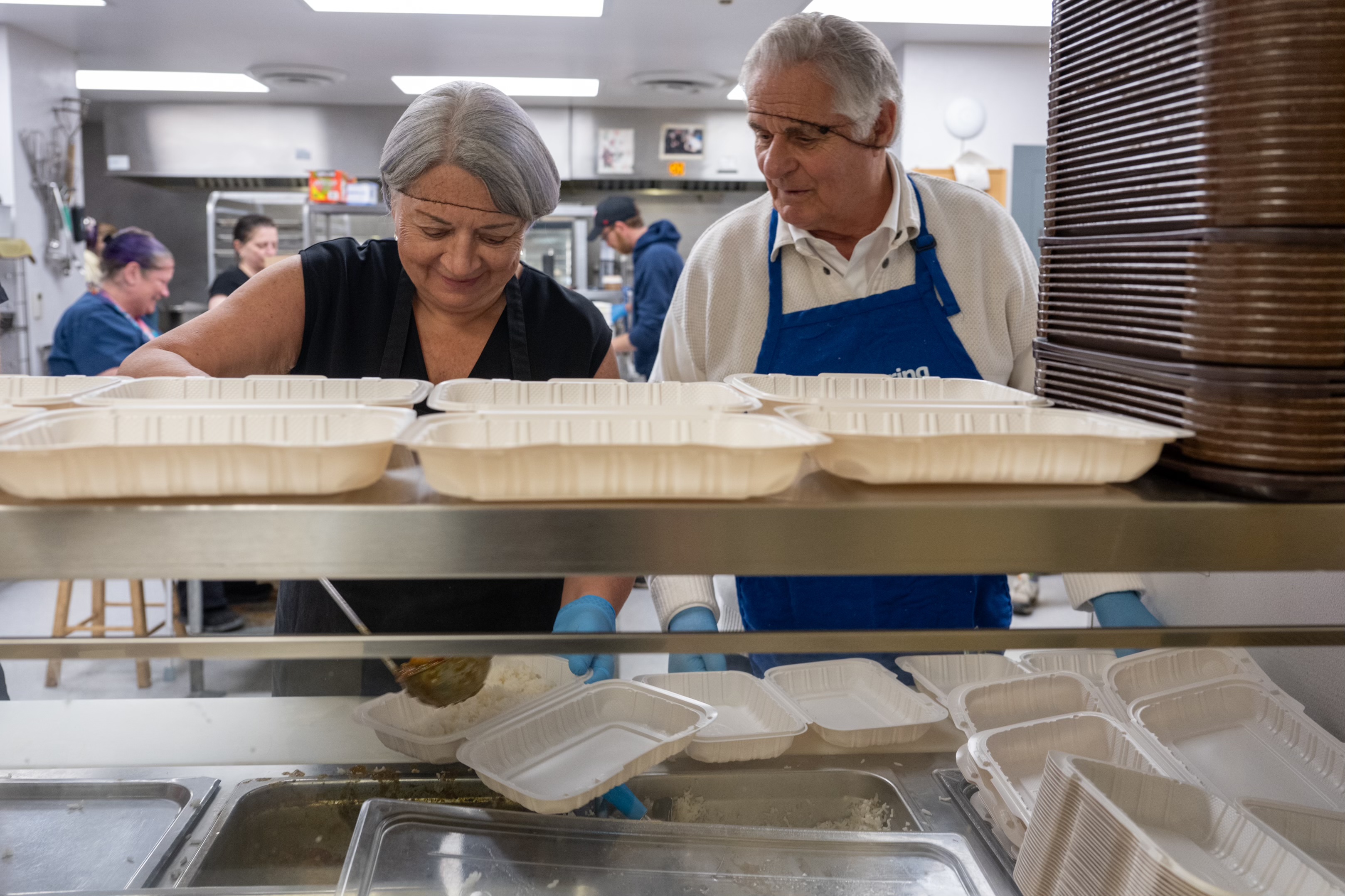 Governor General Simon and Mr. White Fraser working in a kitchen. The Governor General is scooping food into a container.
