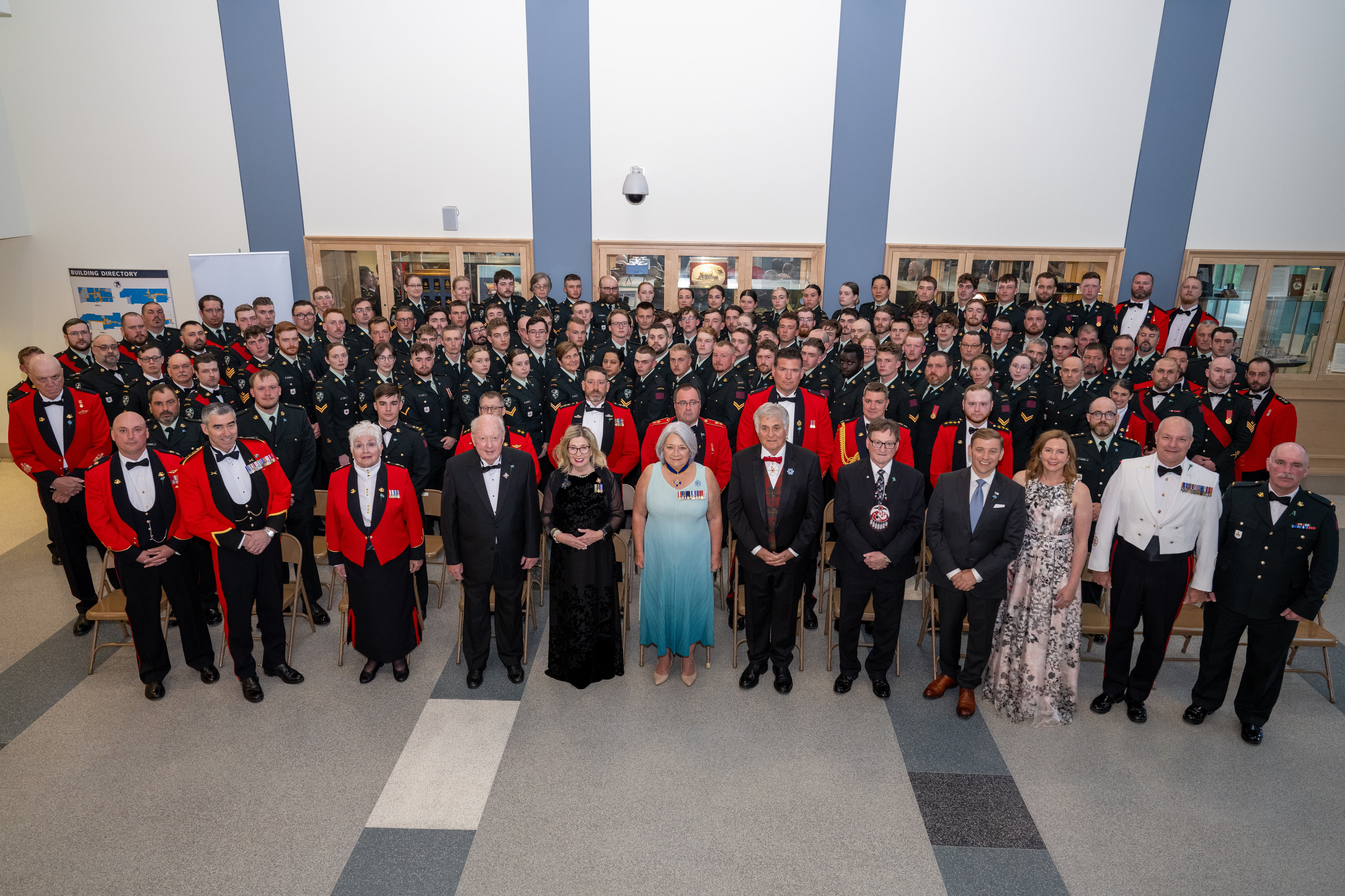 Governor General Simon and Mr. Whit Fraser posing with a large group of people. Everyone is dressed in either formal clothing or uniform. The photo was taken from above.
