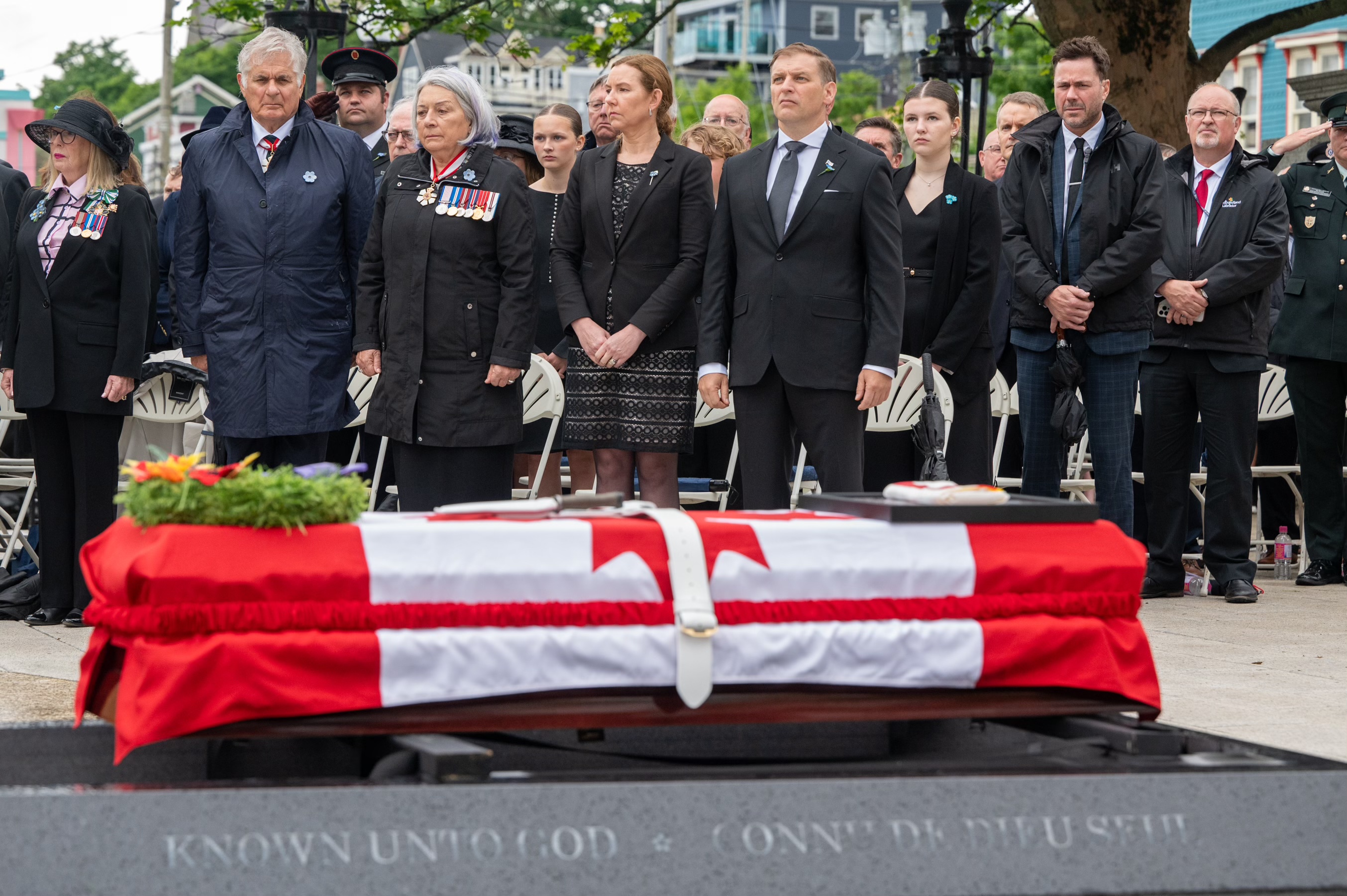 Governor General Simon and Mr. Whit Fraser standing outside with a large group of people at a ceremony. A casket draped with a Canada flag is in the foreground.