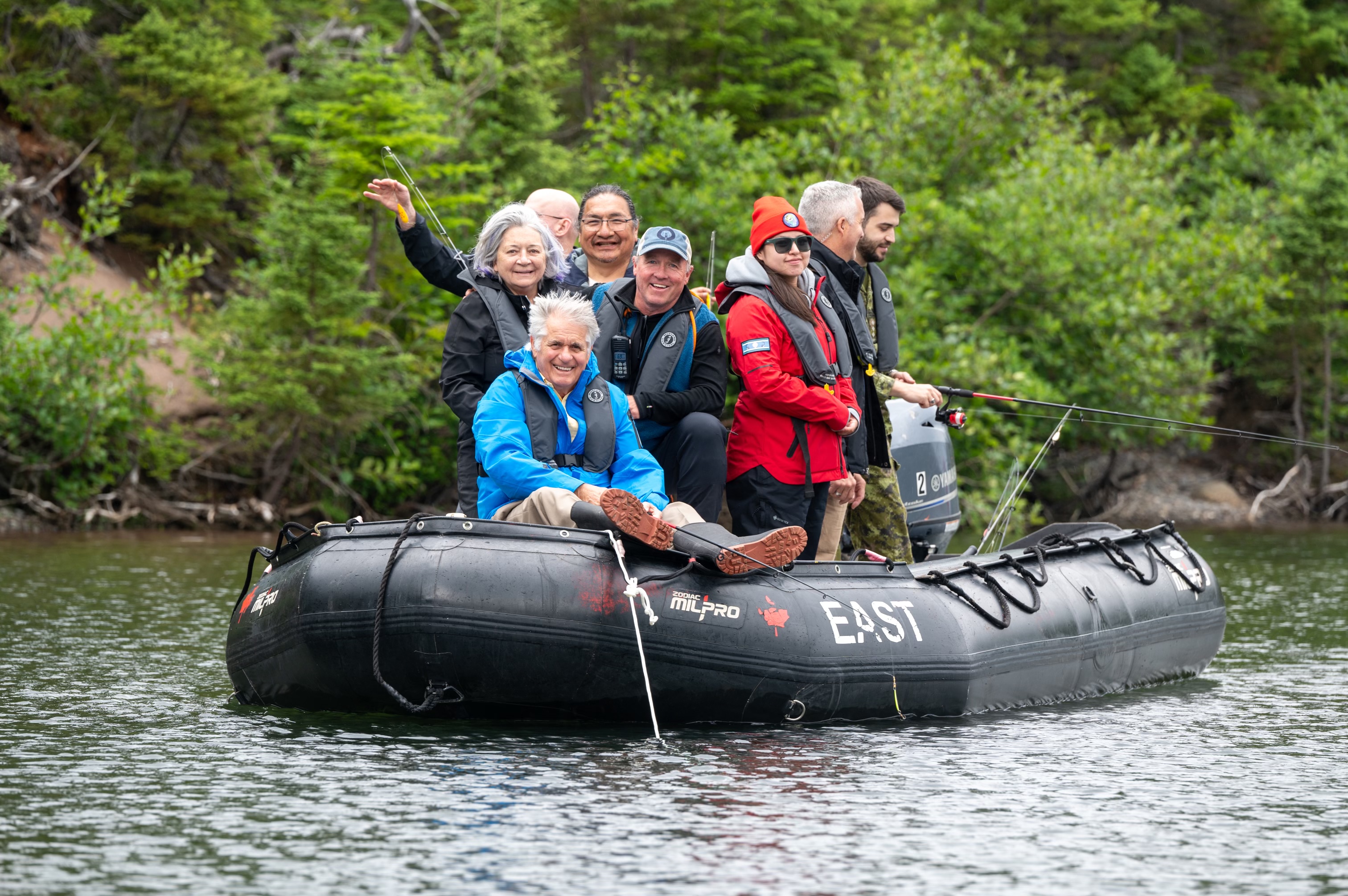 A group of people on a black zodiac. Several of them are fishing.