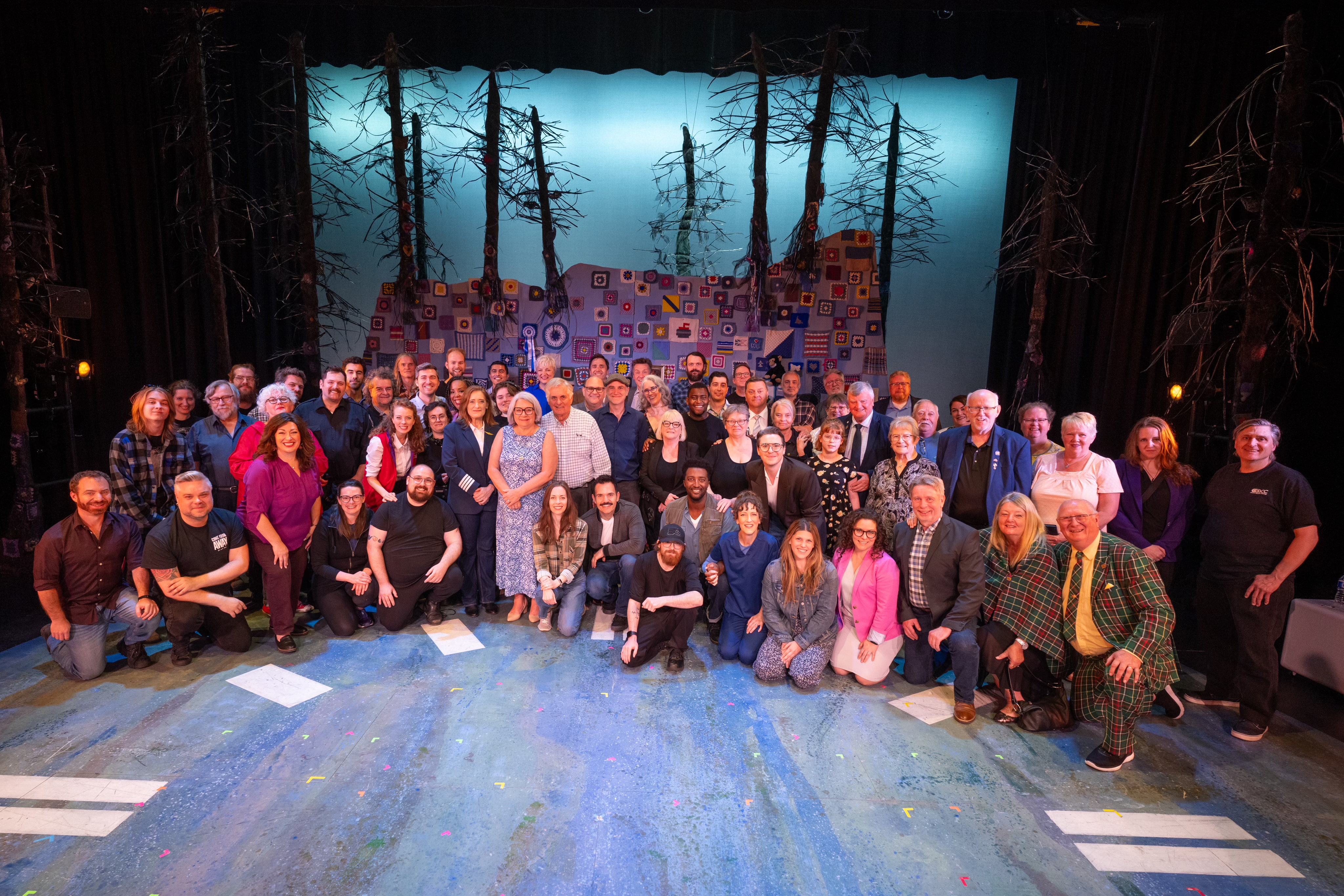 Governor General Mary Simon stands with a large group of people on a stage.