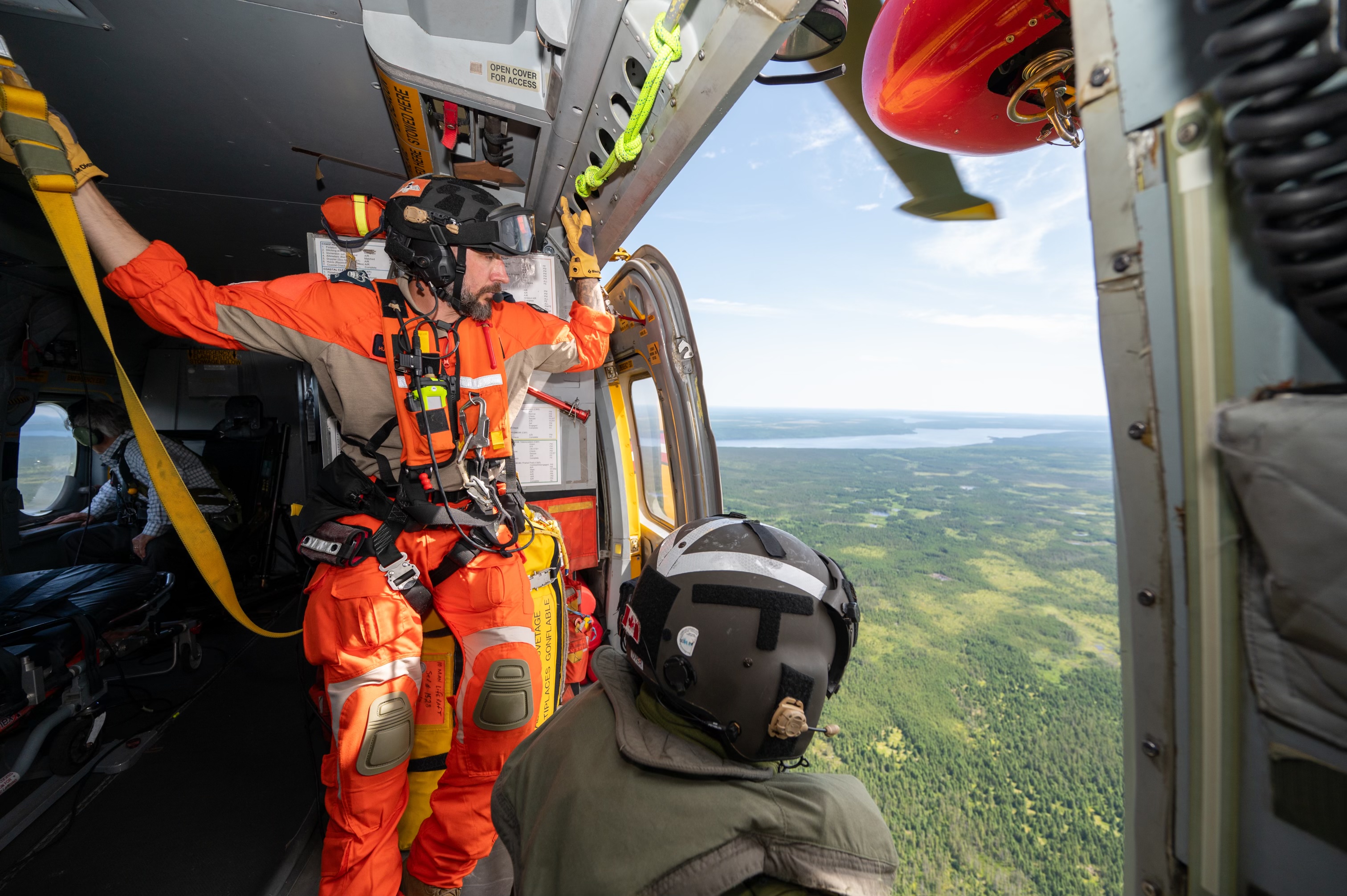 Two members of the Canadian Armed Forces look out from an open door inside a helicopter.