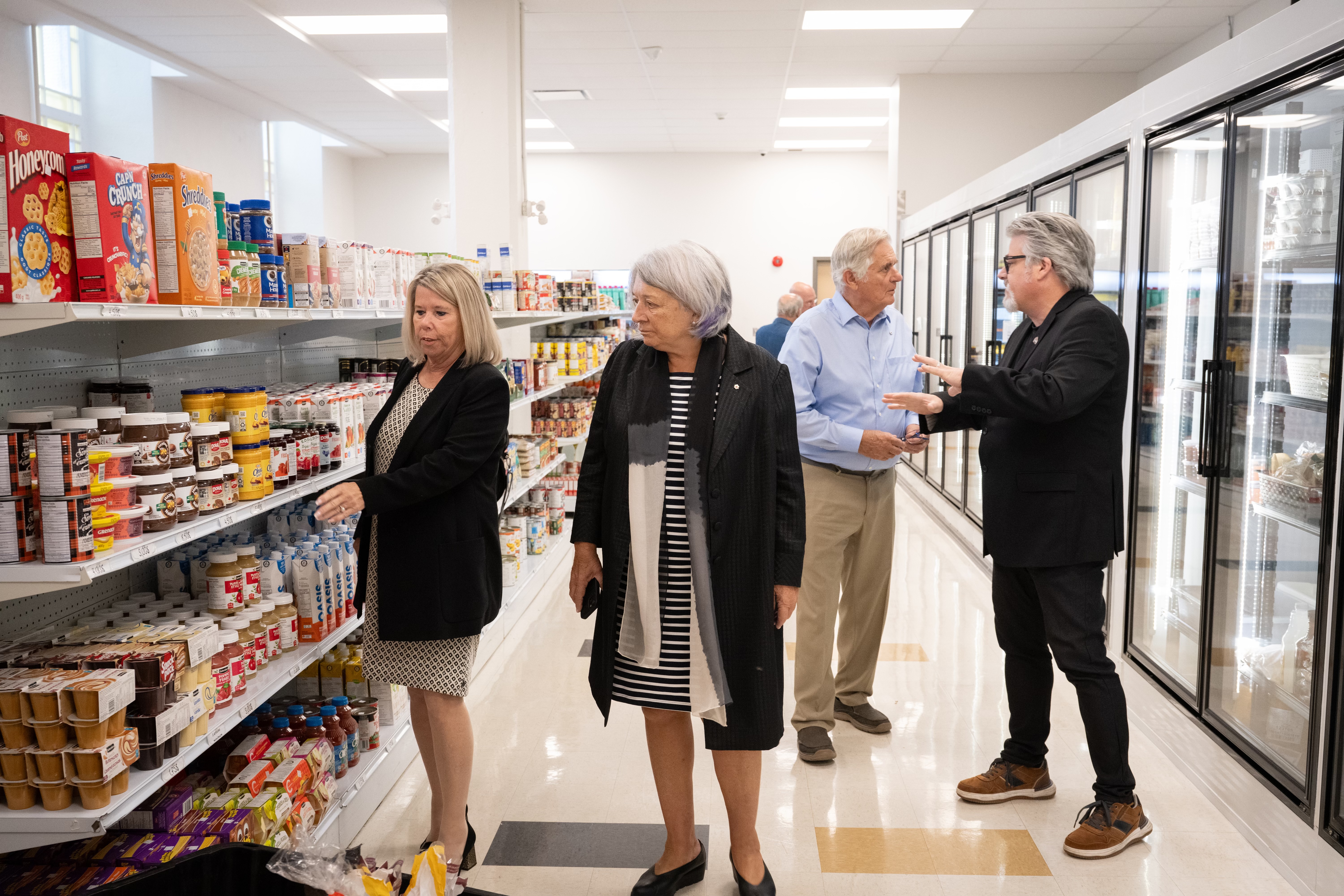 Governor General Simon and Mr. Whit Fraser are walking down a grocery aisle. They are with two other people.