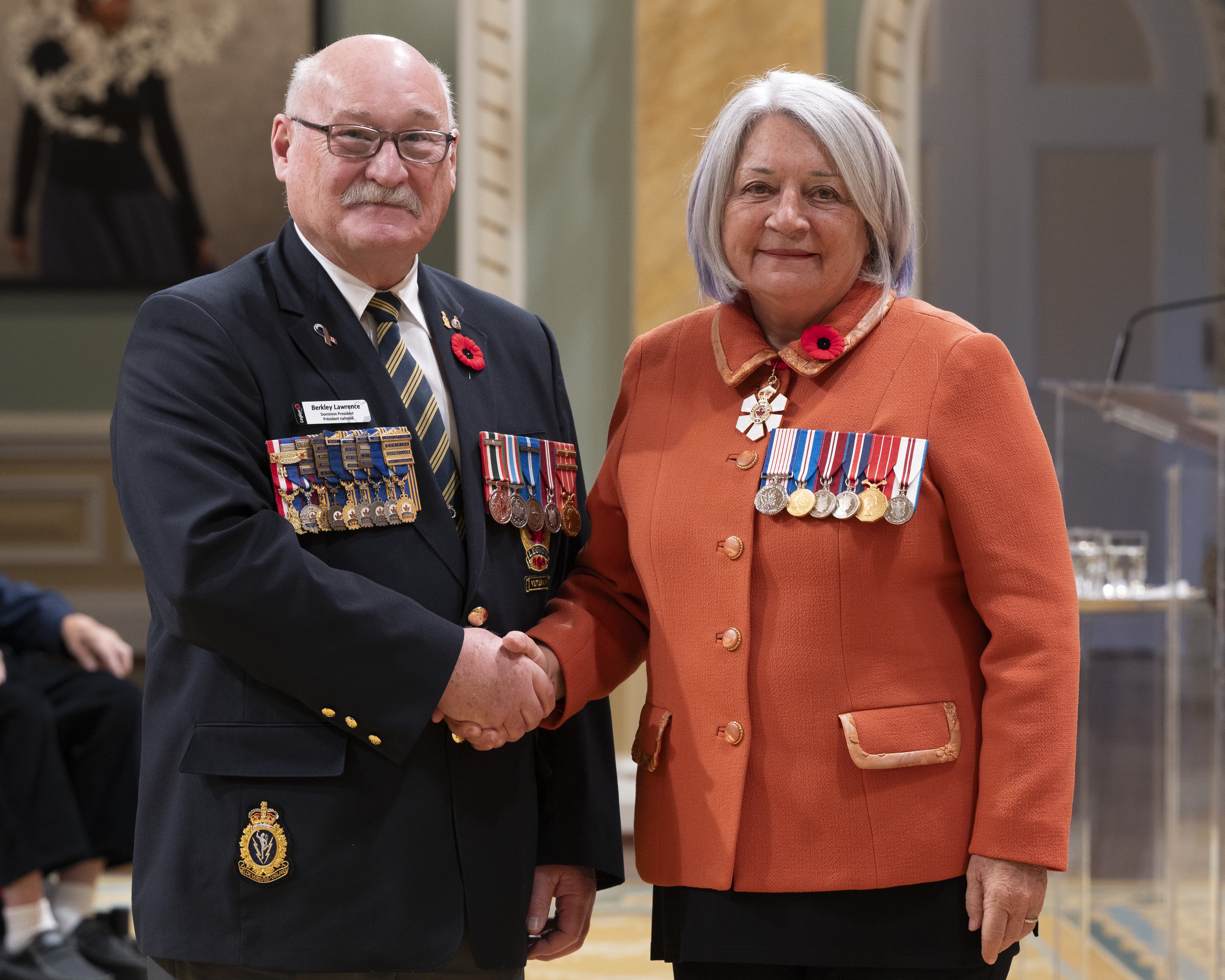 La gouverneure générale Mary Simon à côté de M. Berkley Lawrence, président national de la Légion royale canadienne. Ils portent tous deux des coquelicots et se serrent la main.
