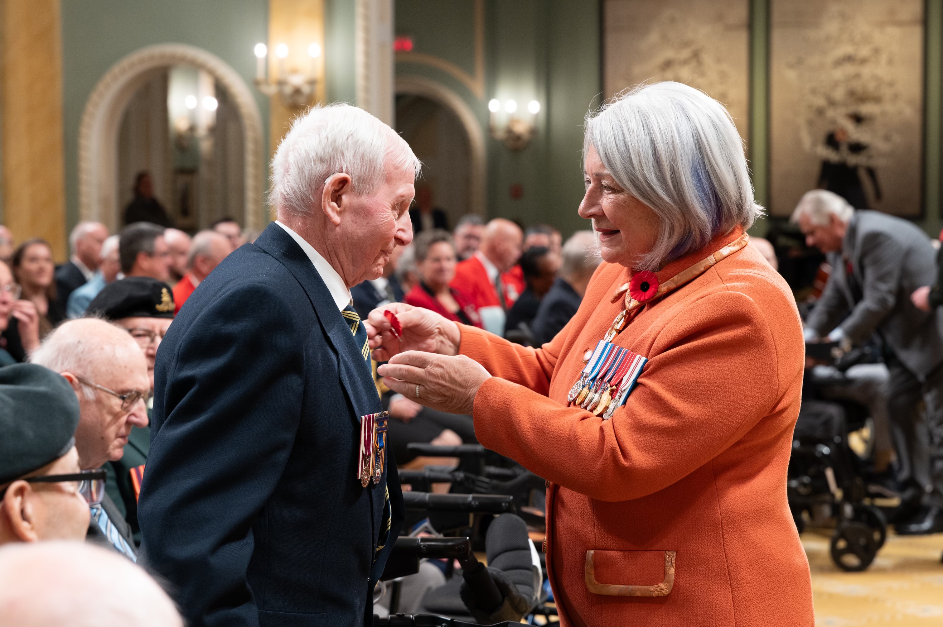La gouverneure générale Mary Simon épingle un coquelicot sur la veste d'un ancien combattant.