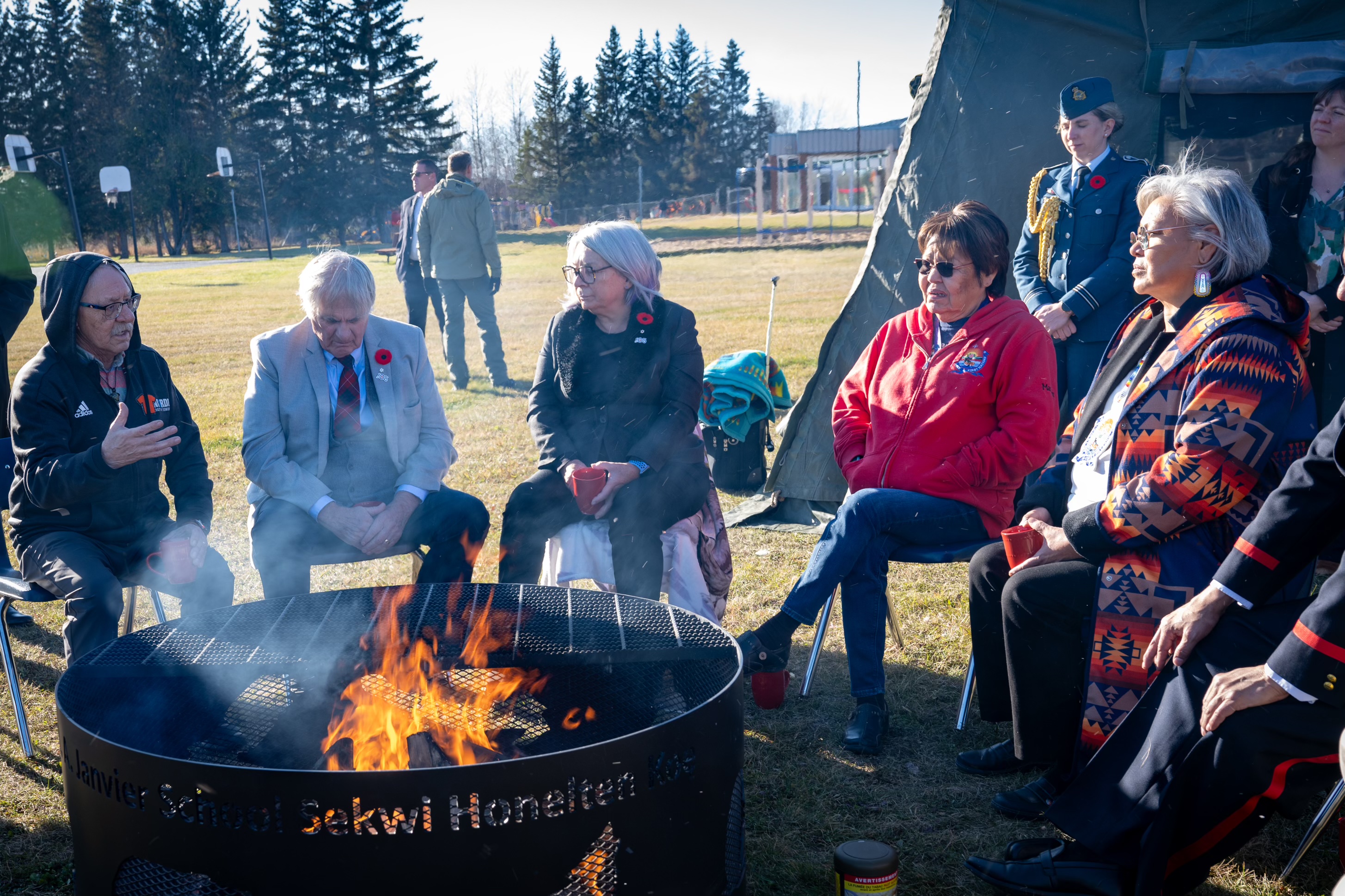 Governor General Mary Simon and Mr. Whit Fraser sitting with a group of people around an open-air fire.