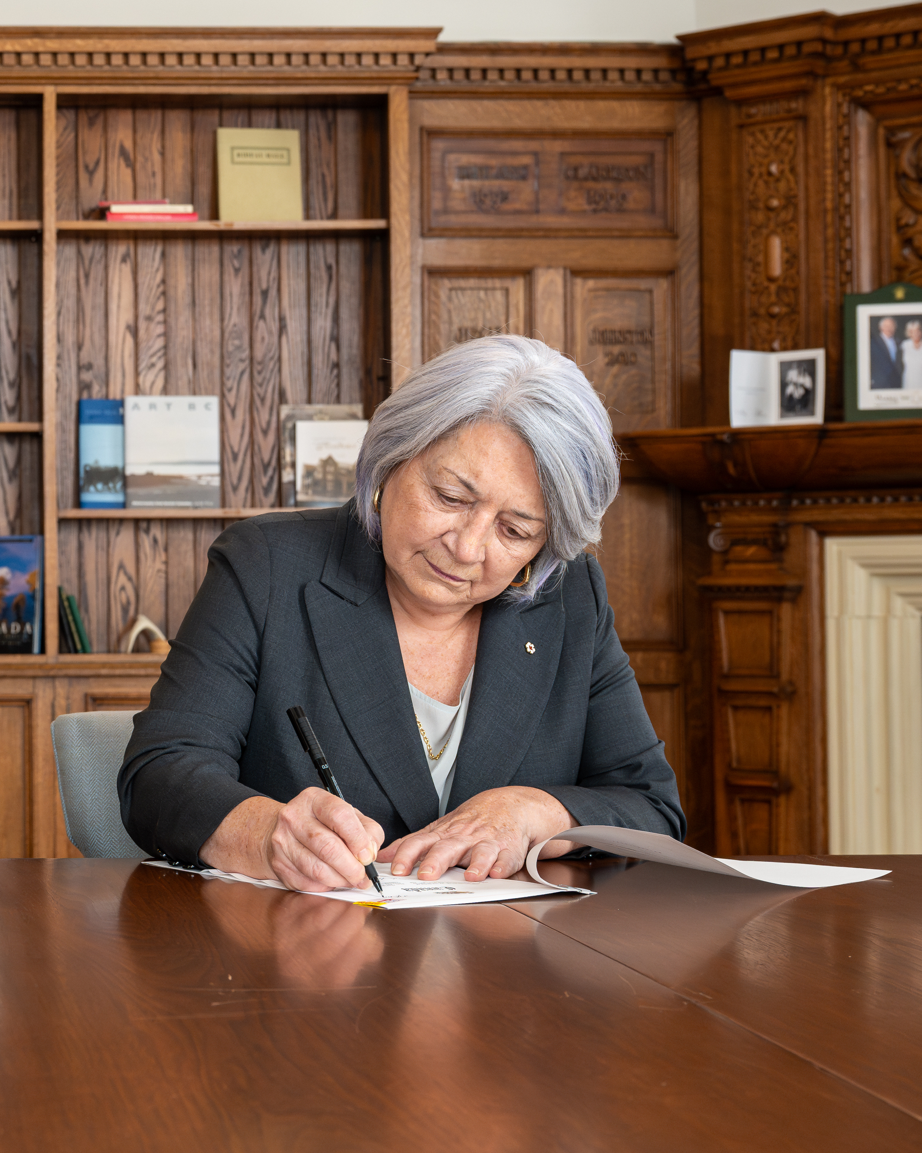 Governor General Mary Simon signing a document at a large wooden table.