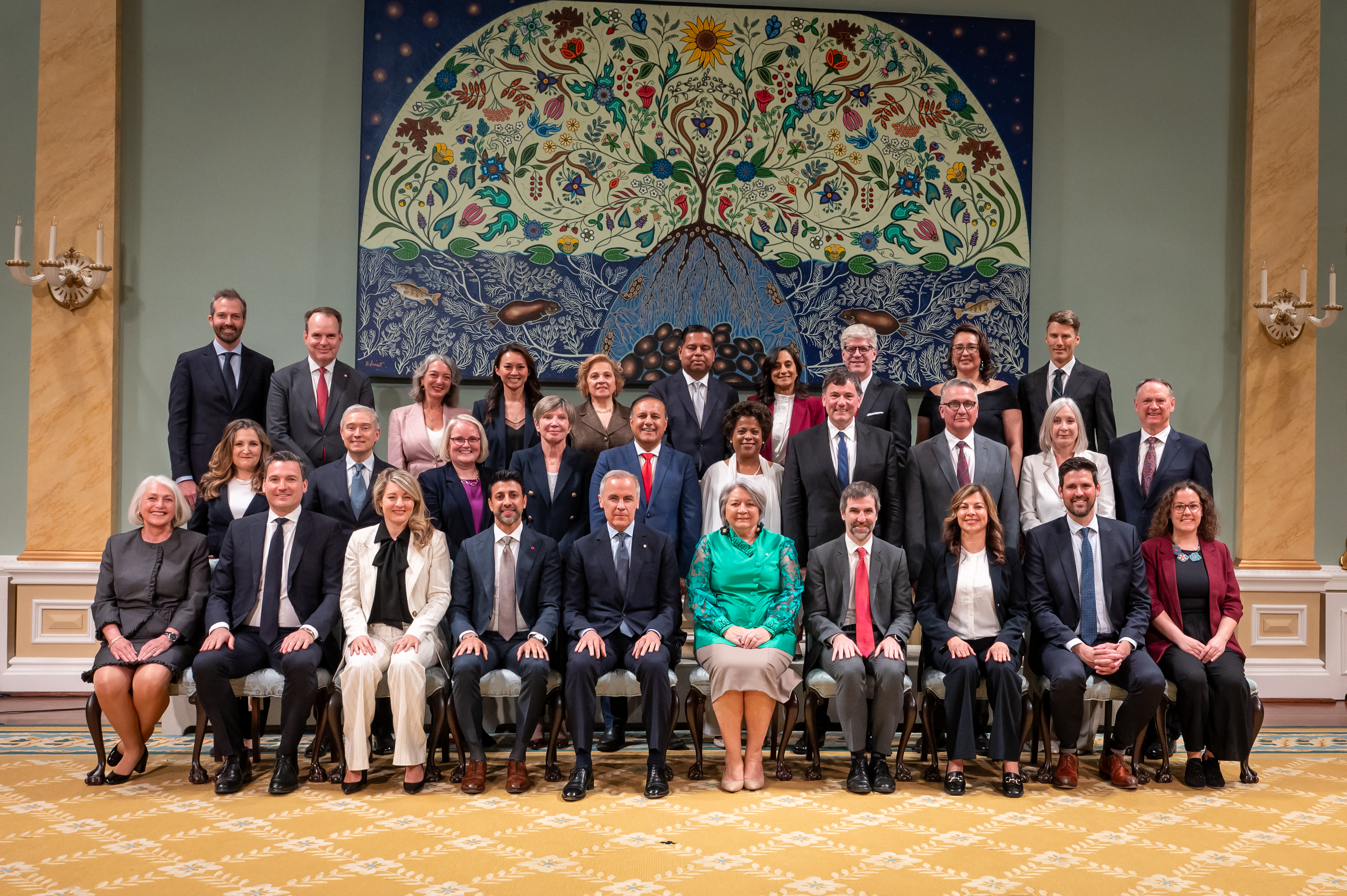 Governor General Simon and Prime Minister Mark Carney sit in the front row of a group photo in the ballroom at Rideau Hall. They are surrounded by members of the new Canadian Ministry.