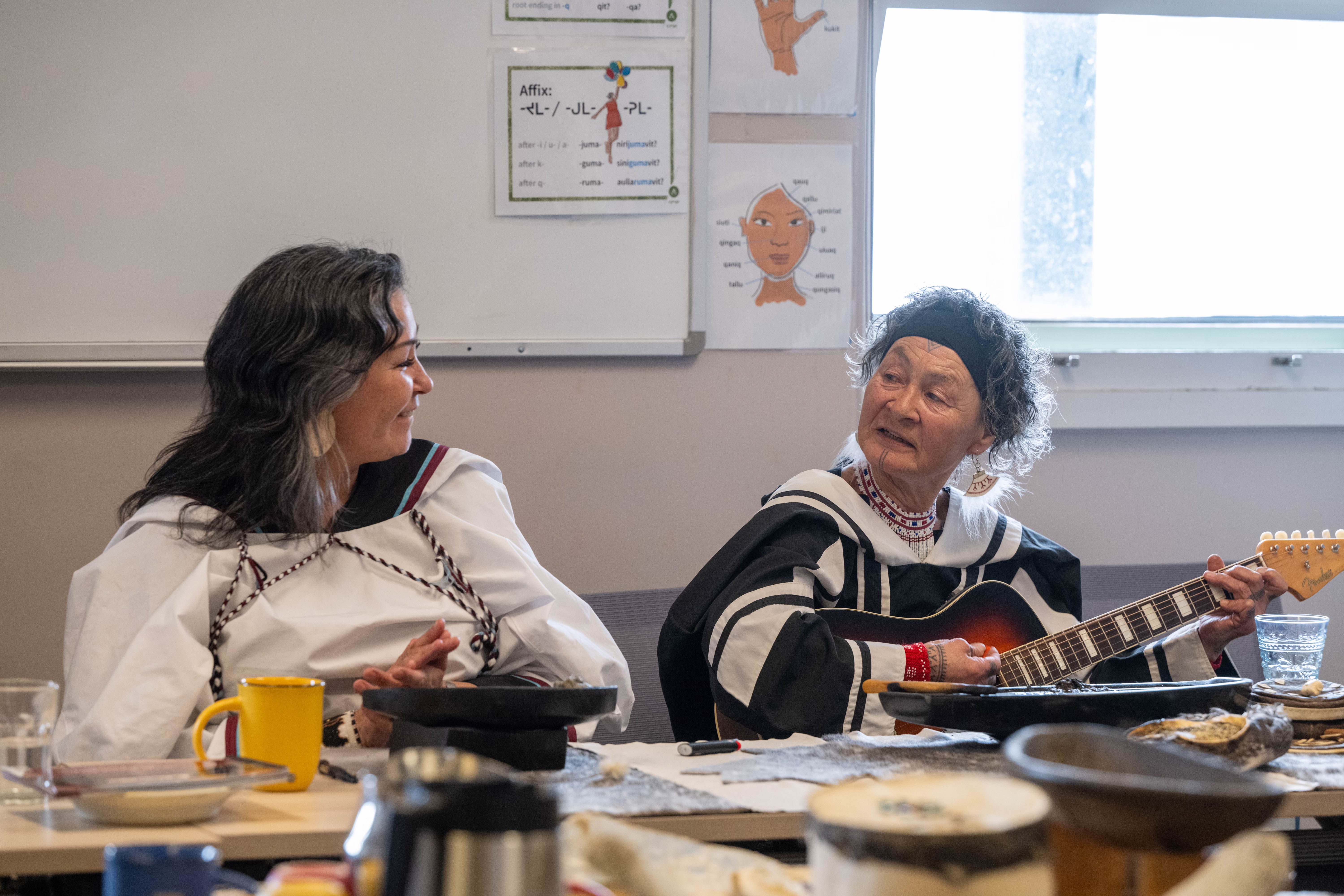 Two Indigenous women perform a song on guitar