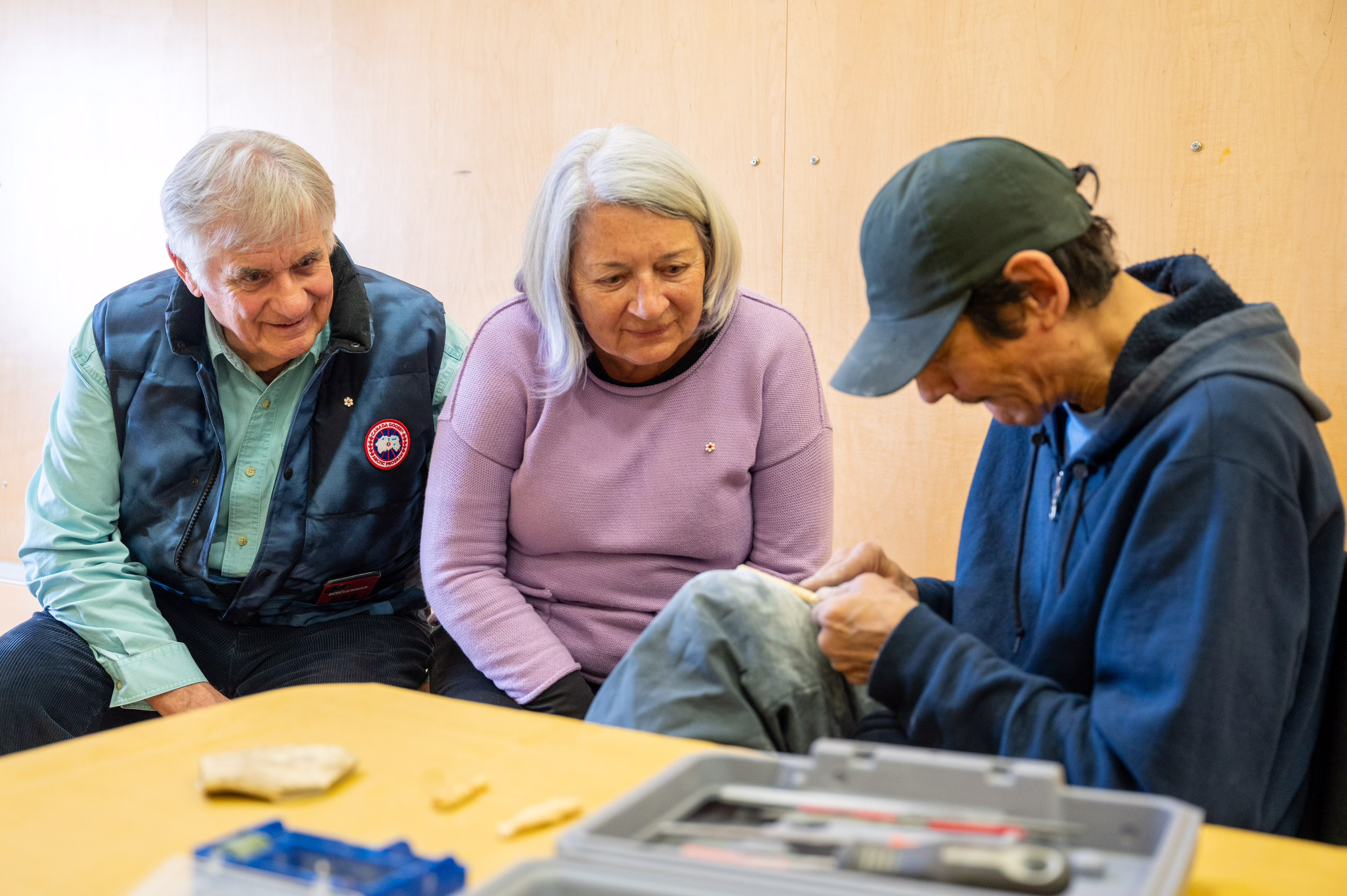 Governor General Mary Simon and Mr. Whit Fraser watch an elder work with small tools on a carving.
