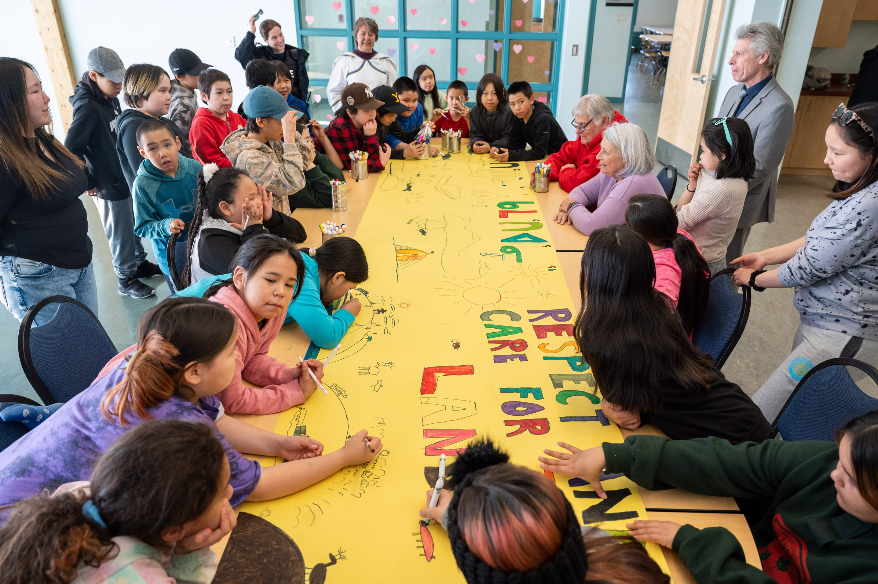 Governor General Mary Simon sits with children to colour a large banner