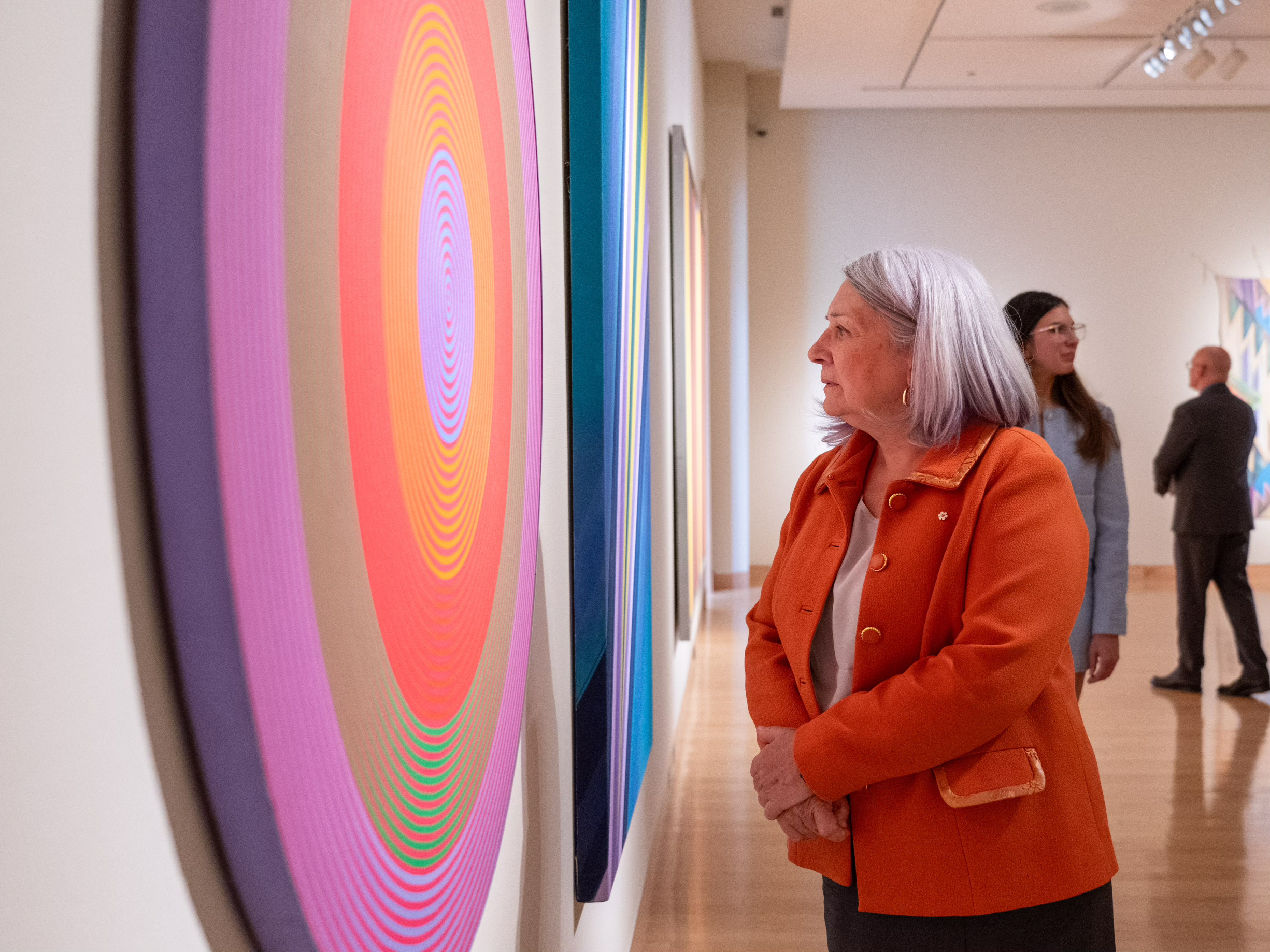 La gouverneure générale Simon inspecte une œuvre d'art colorée accrochée à un mur.