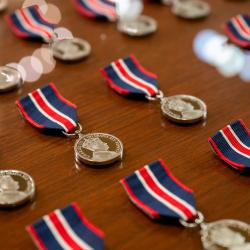 Rows of medals lined up on a table. Each medal is attached to a ribbon using an arrangement of dark blue, bright red and white.