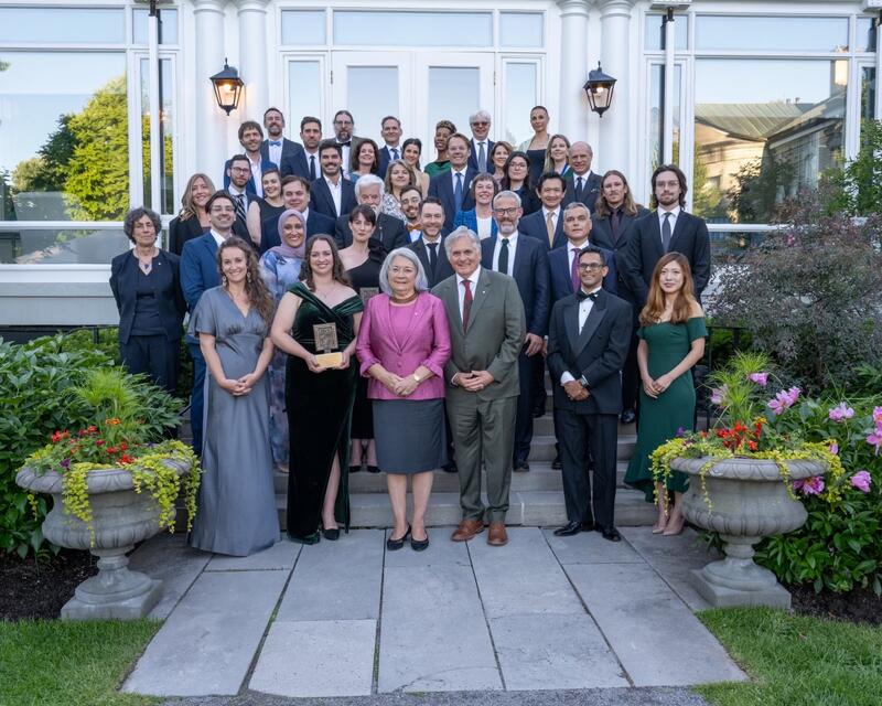 Un groupe de personnes posant pour une photo à l’extérieur. La gouverneure générale Mary Simon et M. Whit Fraser se tiennent au premier rang, au milieu.