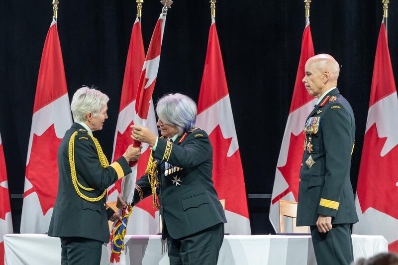 Governor General Mary Simon hands over the Canadian Armed Forces Ensign to General Jennie Carignan. General Wayne Eyre is standing behind her.