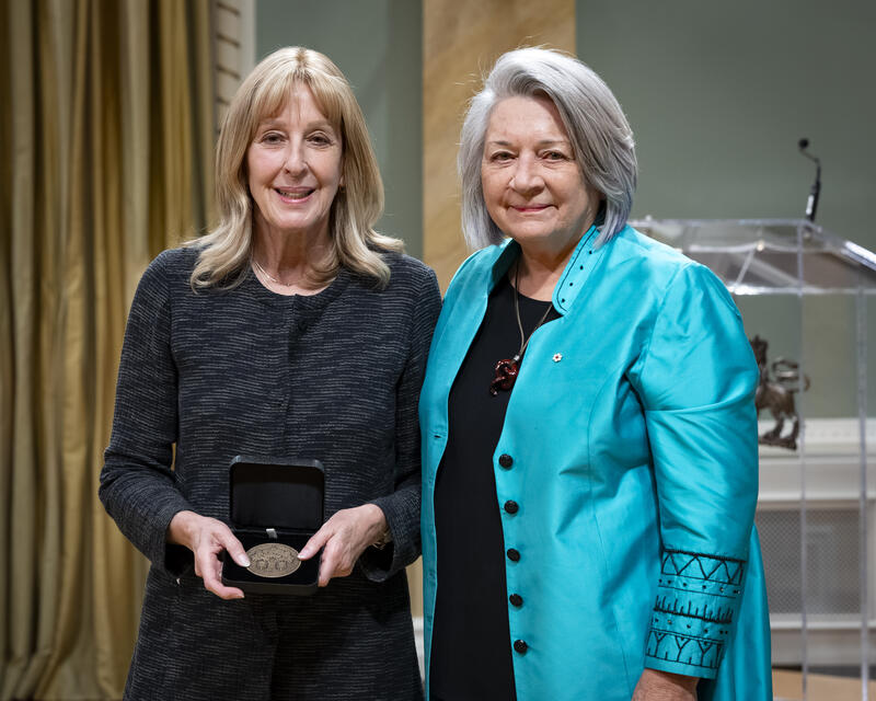 Governor General Mary Simons is posing with a lady who is holding an opened award medal case.