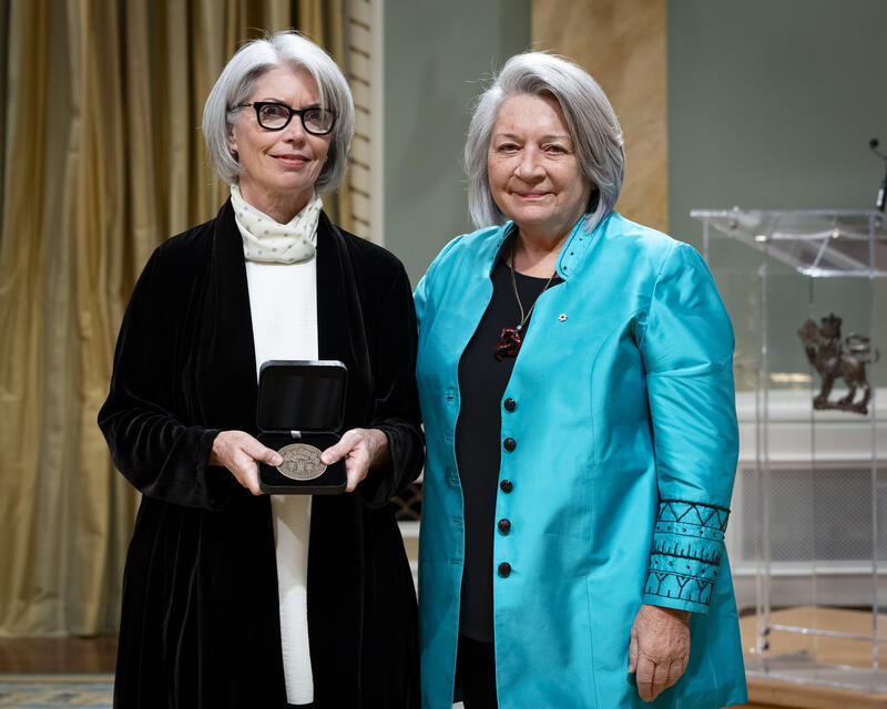 Governor General Mary Simons is posing with a lady who is holding an opened award medal case.