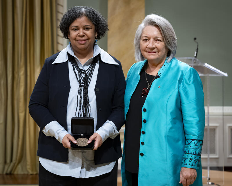 Governor General Mary Simons is posing with a lady who is holding an opened award medal case.