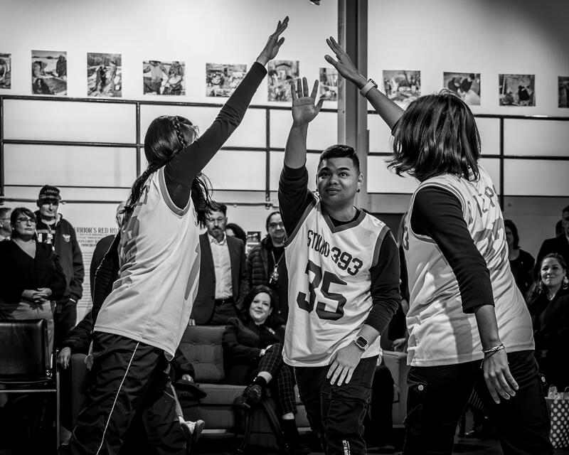 Photo en noir et blanc montrant trois danseurs avec leurs mains droites jointes en l'air. Les danseurs portent tous une tenue de basket-ball.