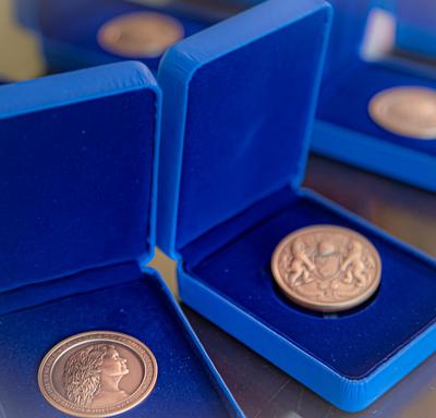 Trois médailles de la Mention élogieuse académique du Gouverneur général pour l'ensemble du Canada exposées dans des boîtes bleues ouvertes sur une table.