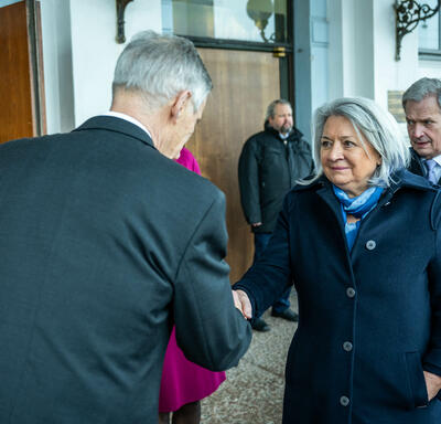 La gouverneure générale Mary Simon serre la main de M. Harry Bogomoloff, président par intérim du conseil municipal. Deux personnes sont debout derrière eux.