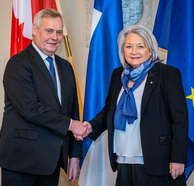 La gouverneure générale Simon serre la main du premier vice-président, Antti Rinne. Derrière eux se trouvent, de gauche à droite, le drapeau du Canada, le drapeau de la Finlande et le drapeau de l’Union européenne.