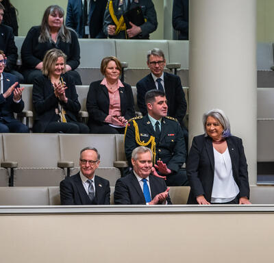 La gouverneure générale Mary Simon est debout sur un balcon du parlement finlandais. Plusieurs parlementaires sont assis autour d’elle. Ils applaudissent.